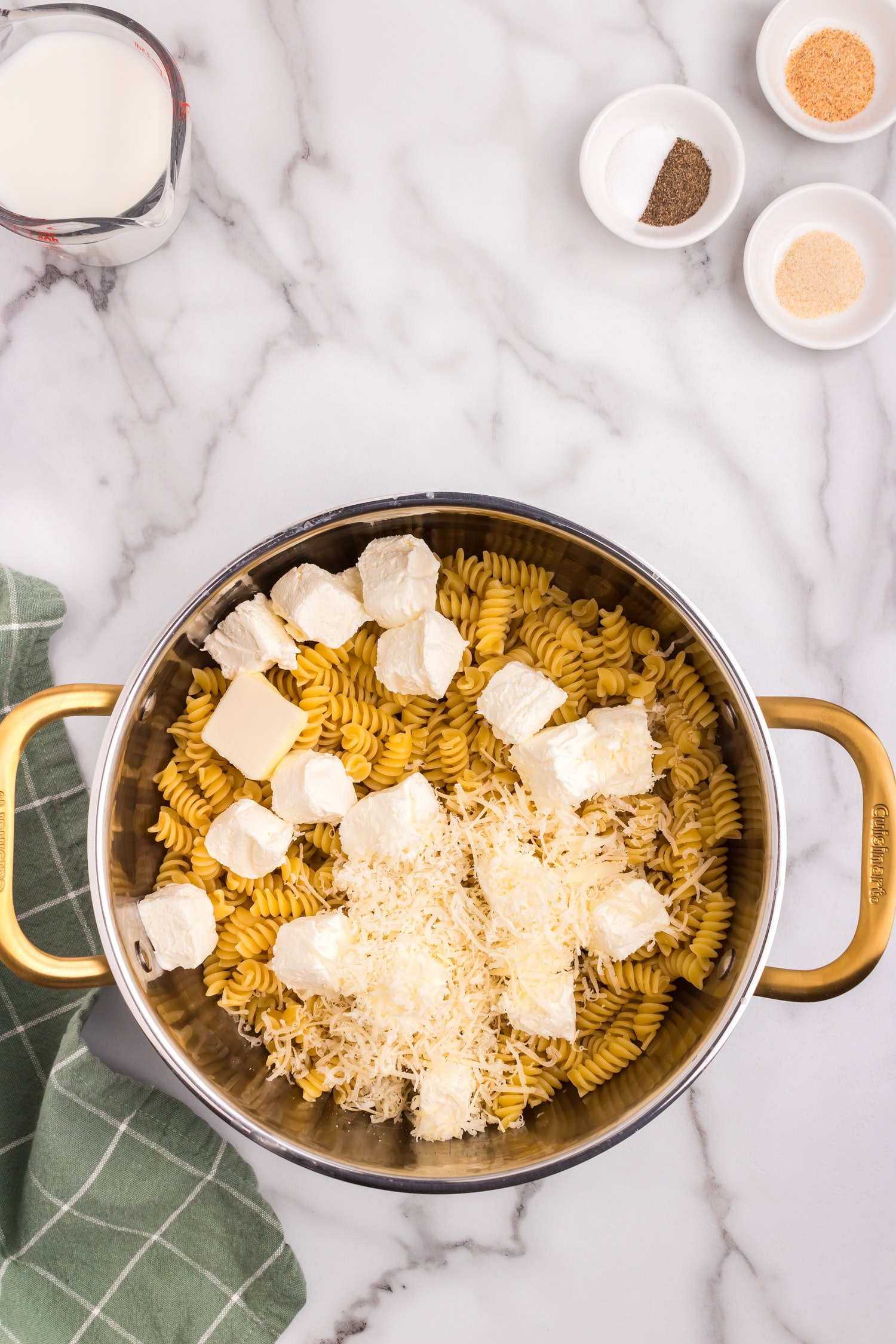 Cream cheese cubes, shredded cheese, and butter placed on top of uncooked rotini pasta inside a pot, ready for cooking.