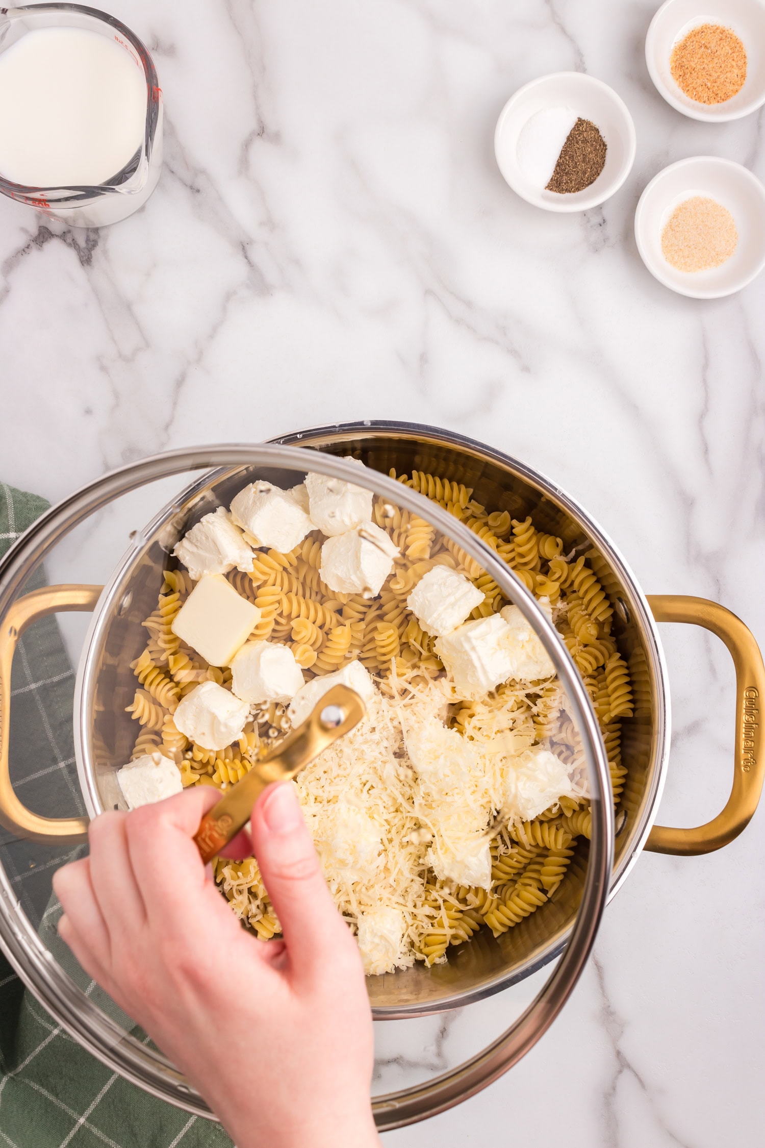 A hand placing a lid on a pot containing pasta, cream cheese, and cheese mixture, preparing it for cooking.