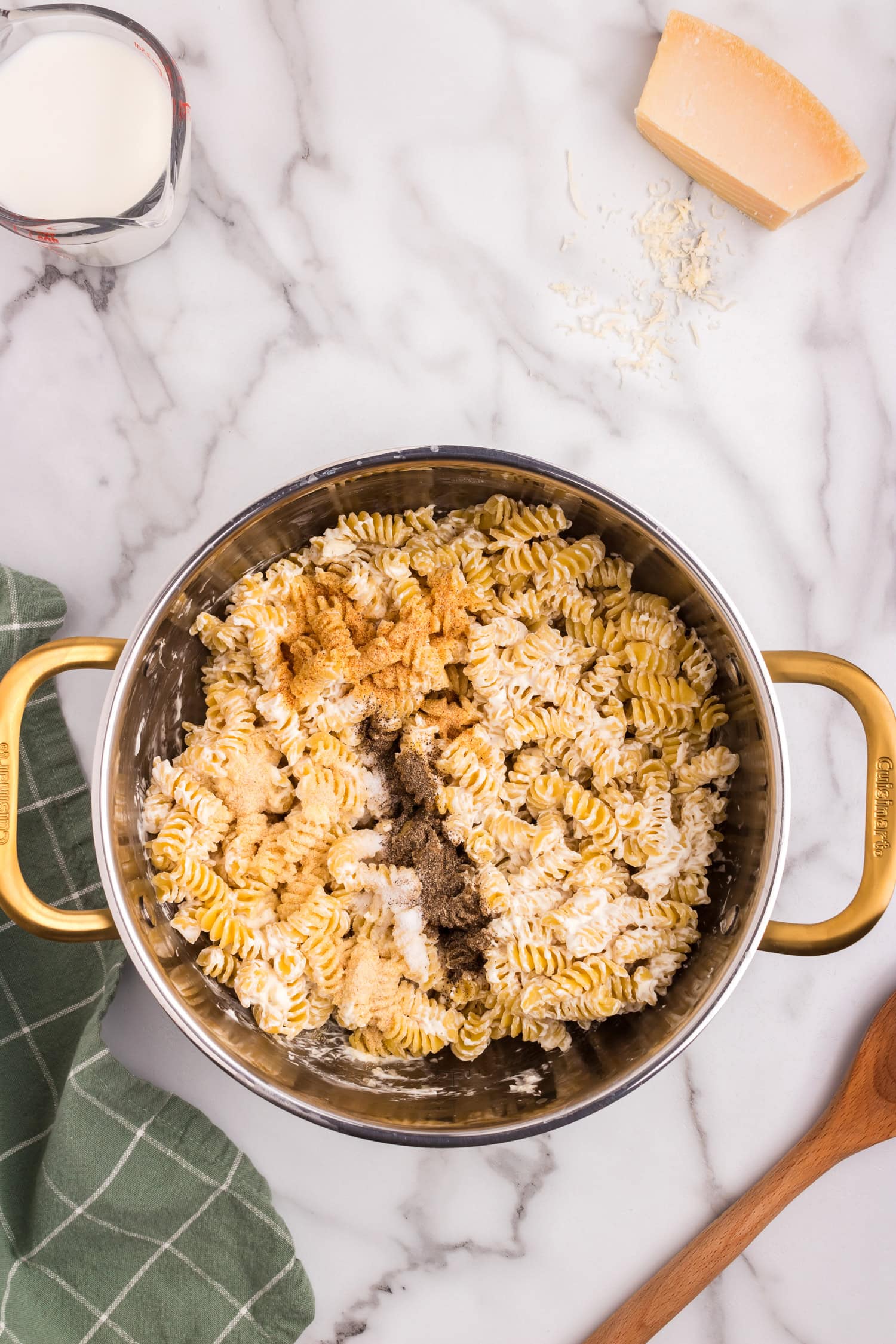Seasonings including salt, pepper, garlic powder, and onion powder sprinkled over partially mixed creamy rotini pasta in a pot.