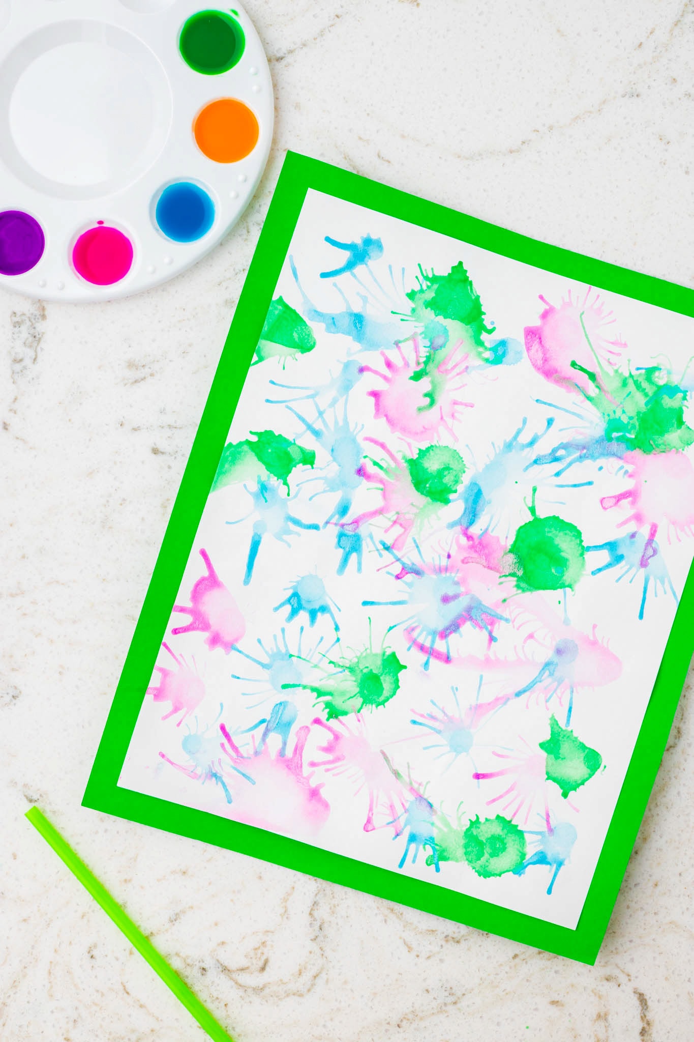 The same artwork as Image 7, now bordered with a bright green frame. A paint palette and green straw rest nearby on the marble surface.
