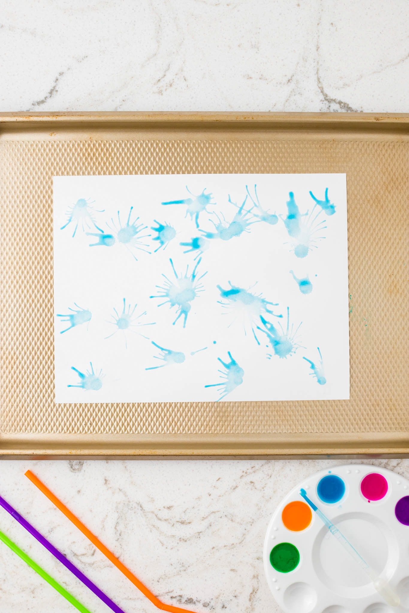The same piece of paper from Image 3, now with blue paint blown into radial streaks using the straw blow technique.