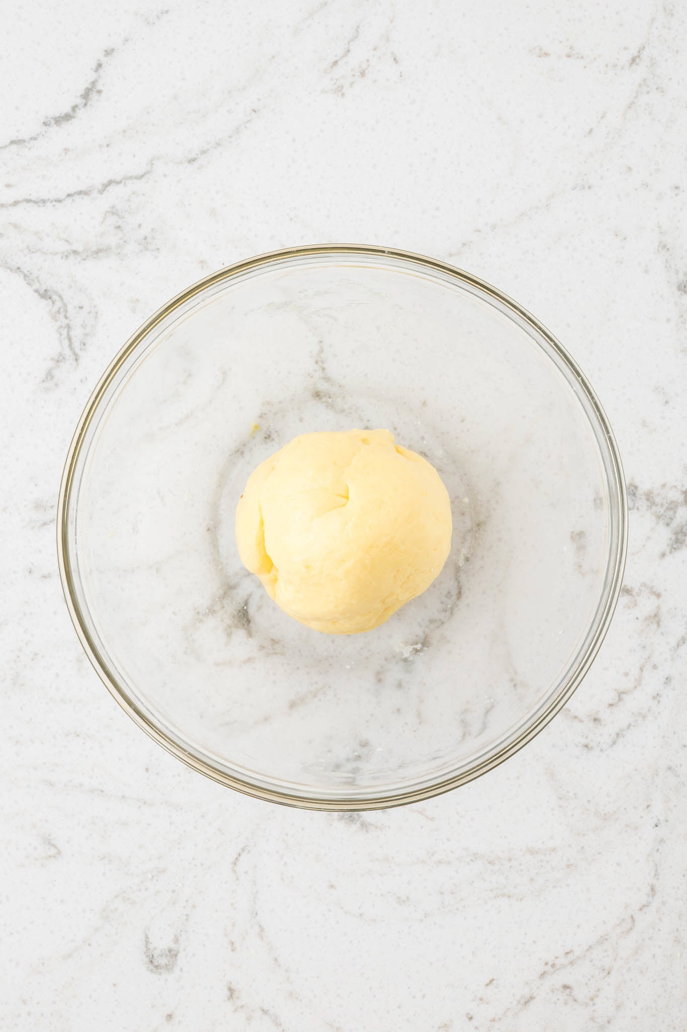 A smooth, cohesive ball of banana pudding slime after thorough kneading, resting in a clean glass bowl.