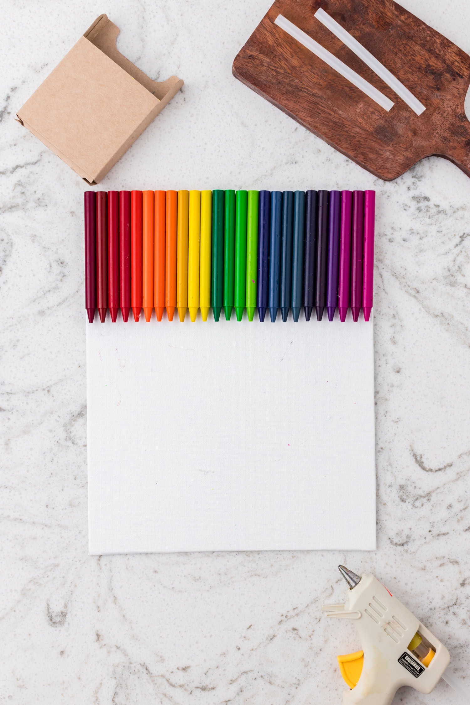 All the crayons, arranged in a full rainbow spectrum from red to purple, are now glued along the top edge of the canvas.