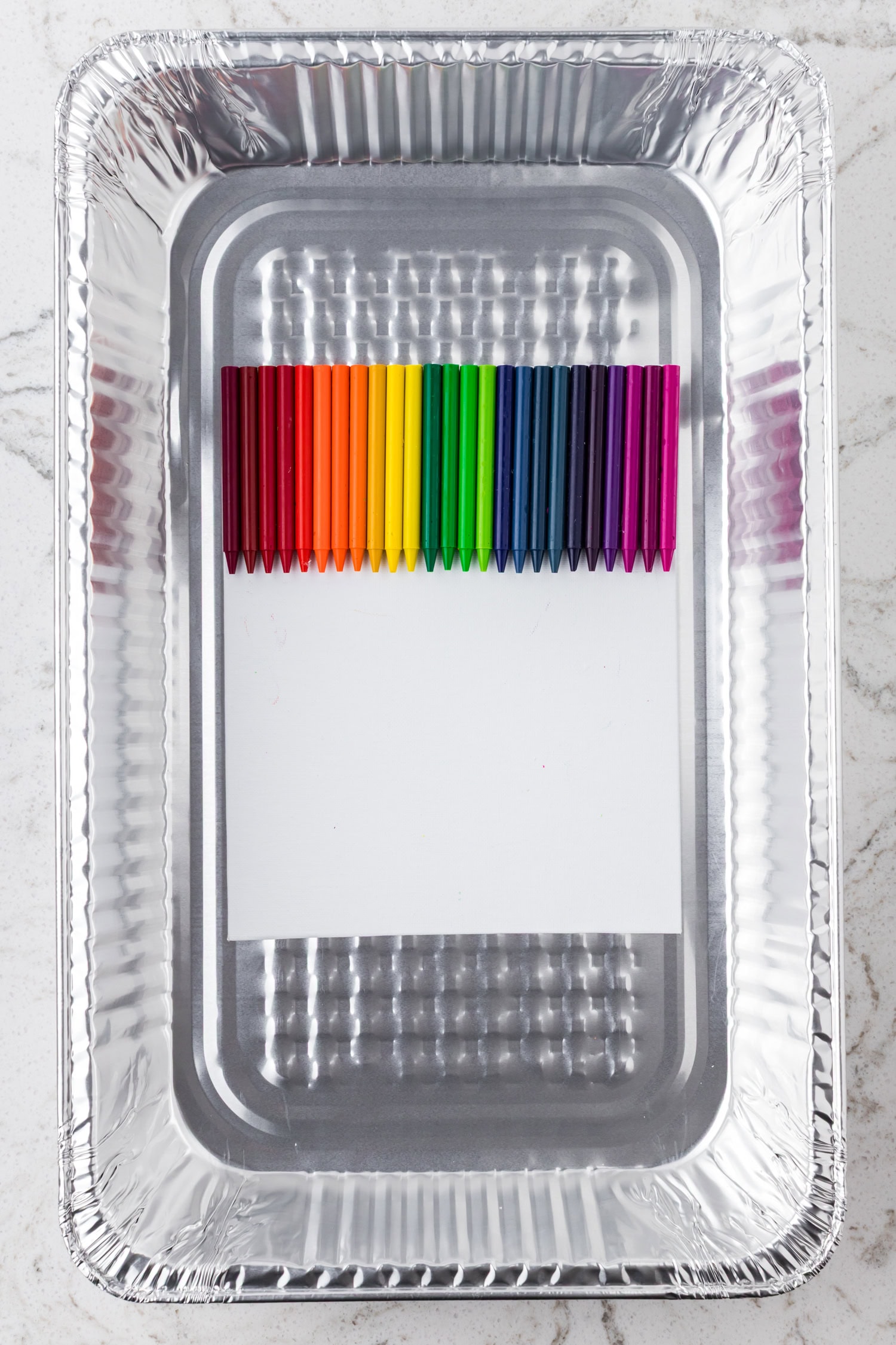 The crayon-adorned canvas is placed inside a large aluminum tray, ready for heat application.