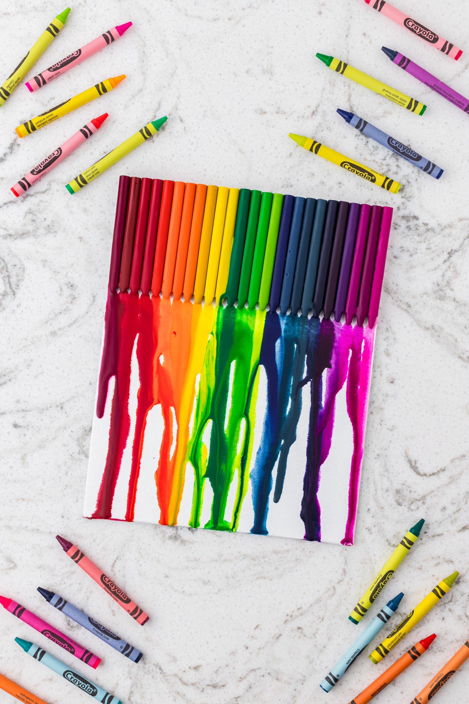 The finished melted crayon art piece lies flat on a surface, surrounded by various crayons.


