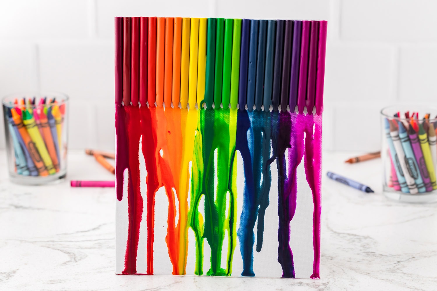 The final artwork stands vertically, showcasing a vivid rainbow of melted wax drips, with crayon tips still attached at the top.