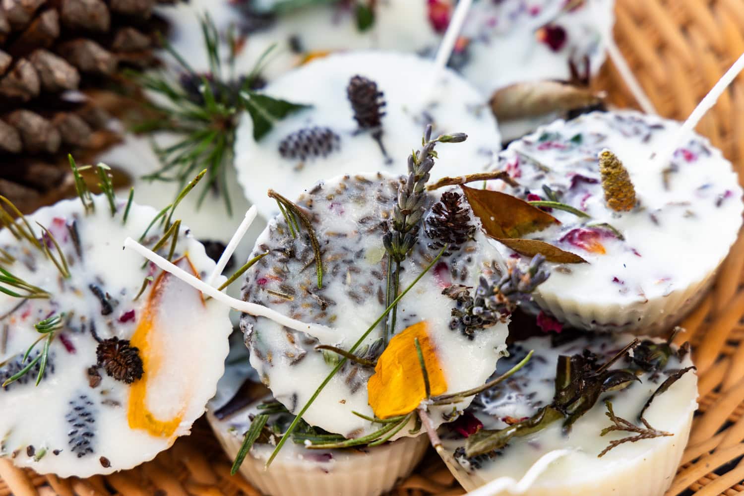 A close-up of the campfire starters in the basket, showing detail of the natural elements embedded in the wax, such as lavender, petals, pine sprigs, and cones.