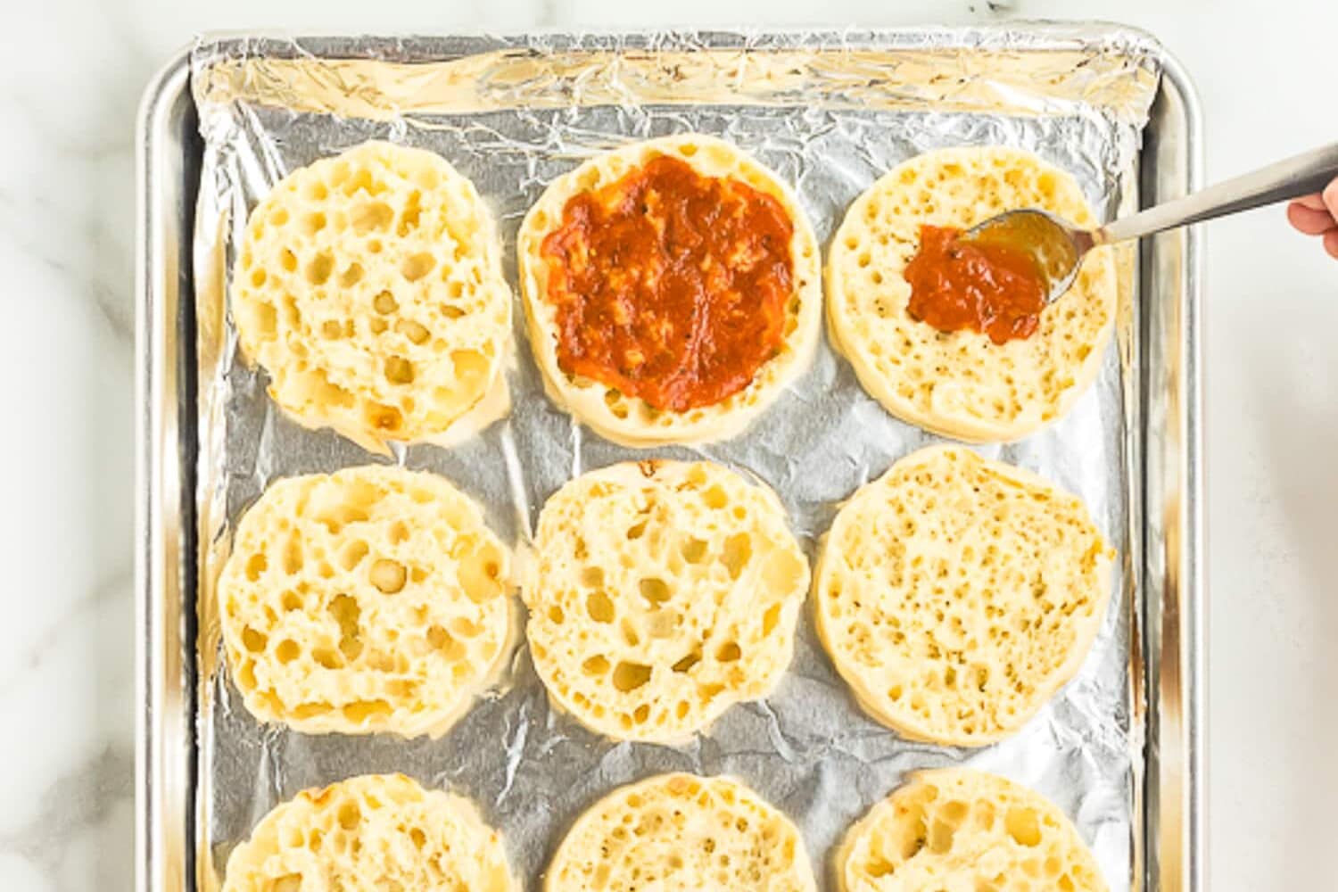 Sheet pan with English muffins topped with pizza sauce