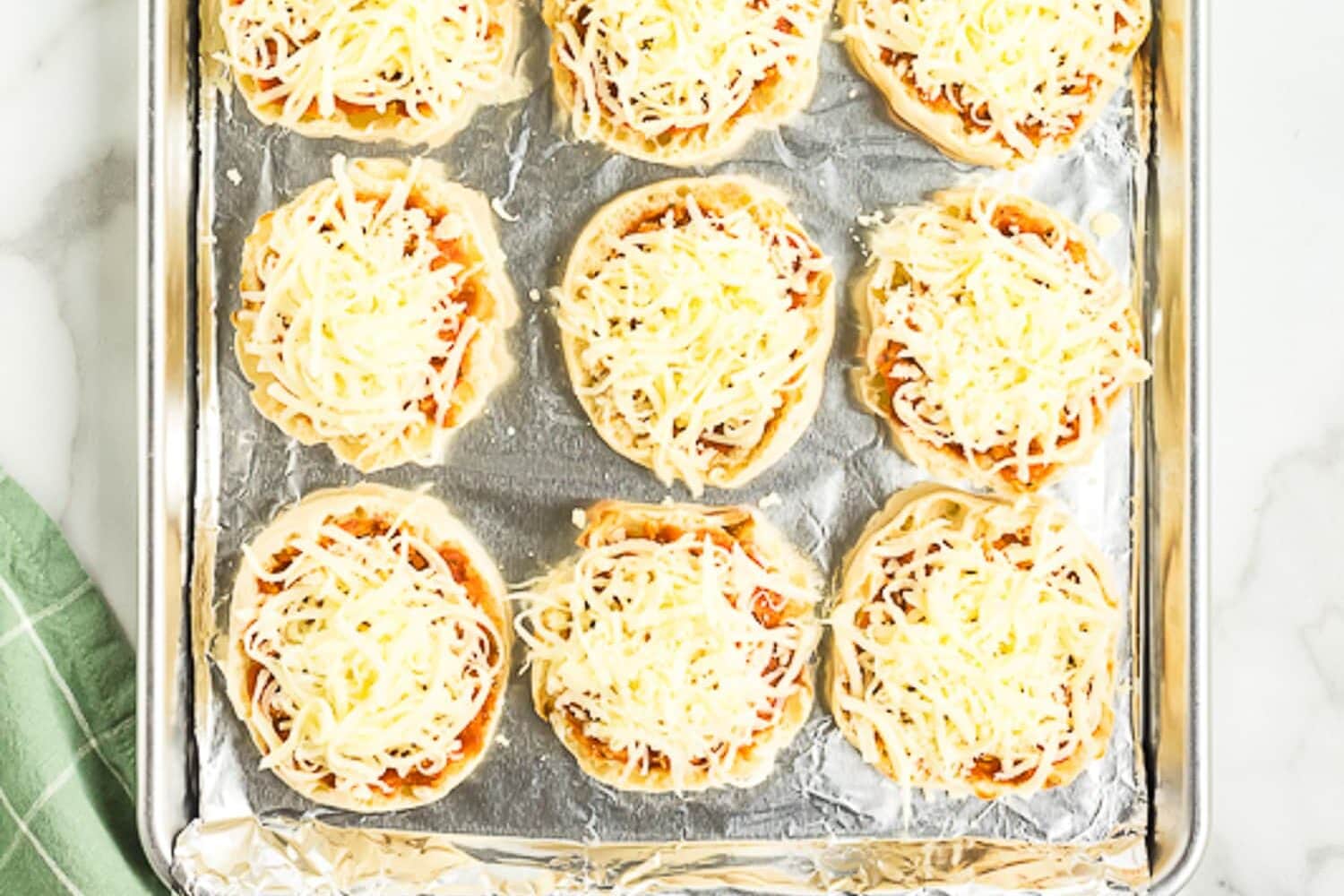 Sheet pan with English muffins topped with Mozzarella cheese