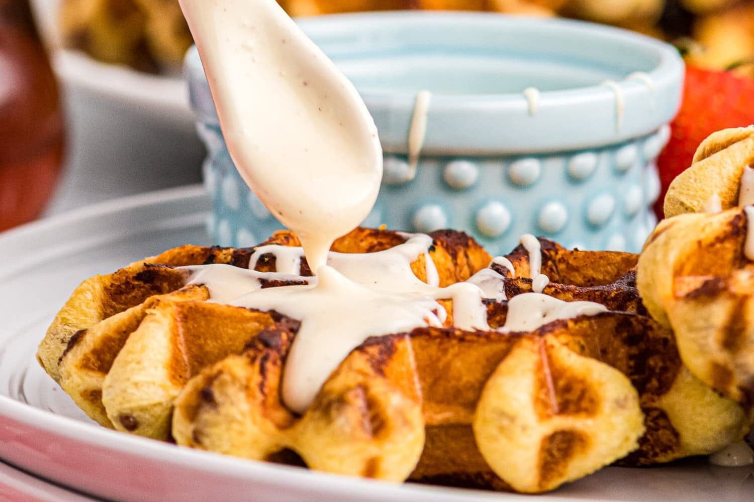 Drizzling cream cheese glaze on cinnamon roll made in waffle maker
