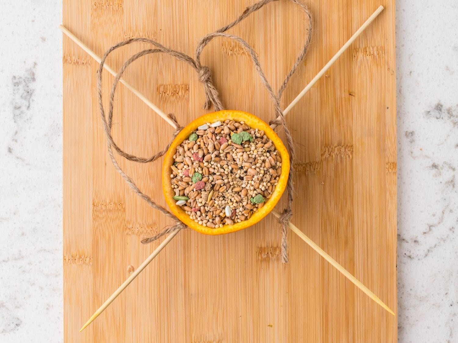 The completed orange bird feeder filled with bird seed, ready for hanging.