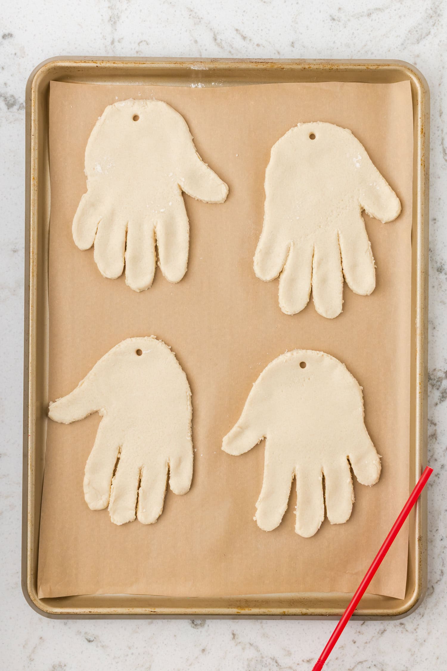 Four handprint-shaped salt dough ornaments on a baking sheet lined with parchment paper, each with a hole for hanging.