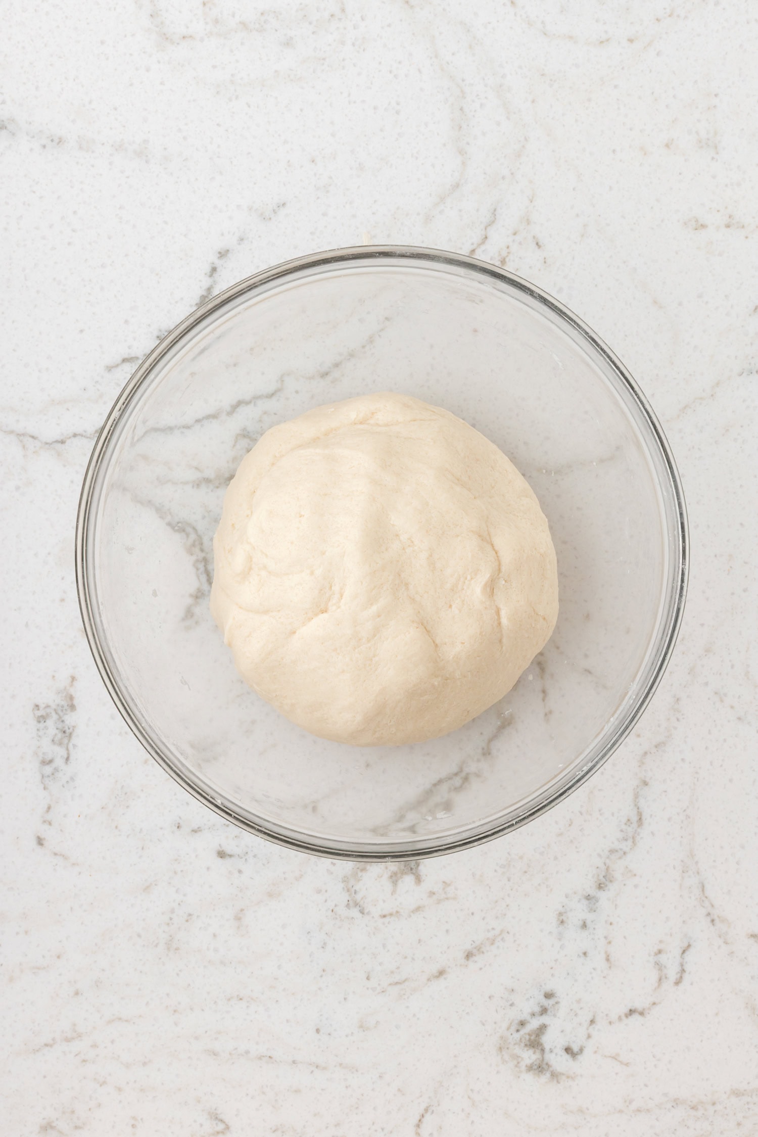 Ball of smooth salt dough resting in a glass bowl on a marble countertop.