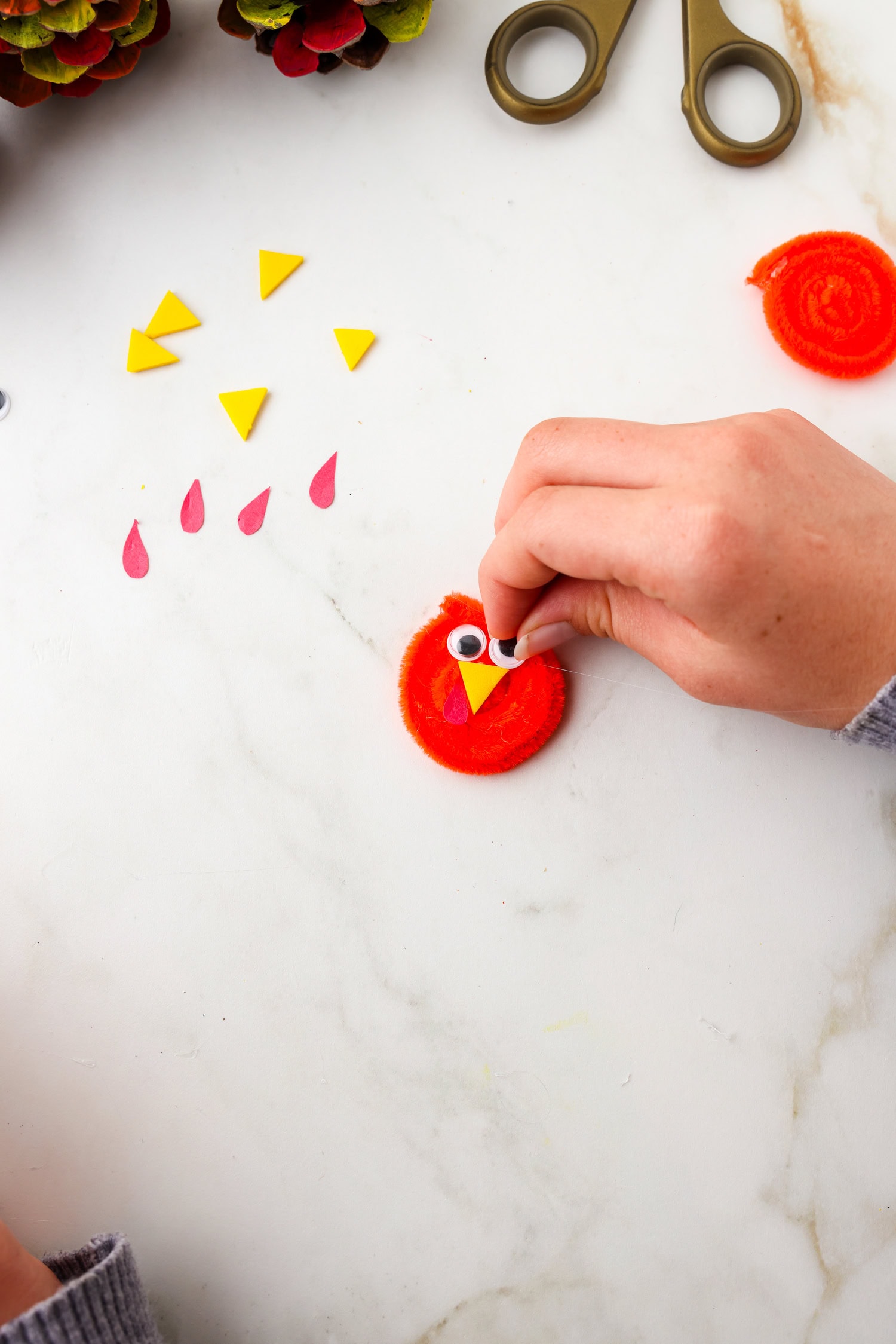 Picture of googly eyes being glued onto pipecleaner face.
