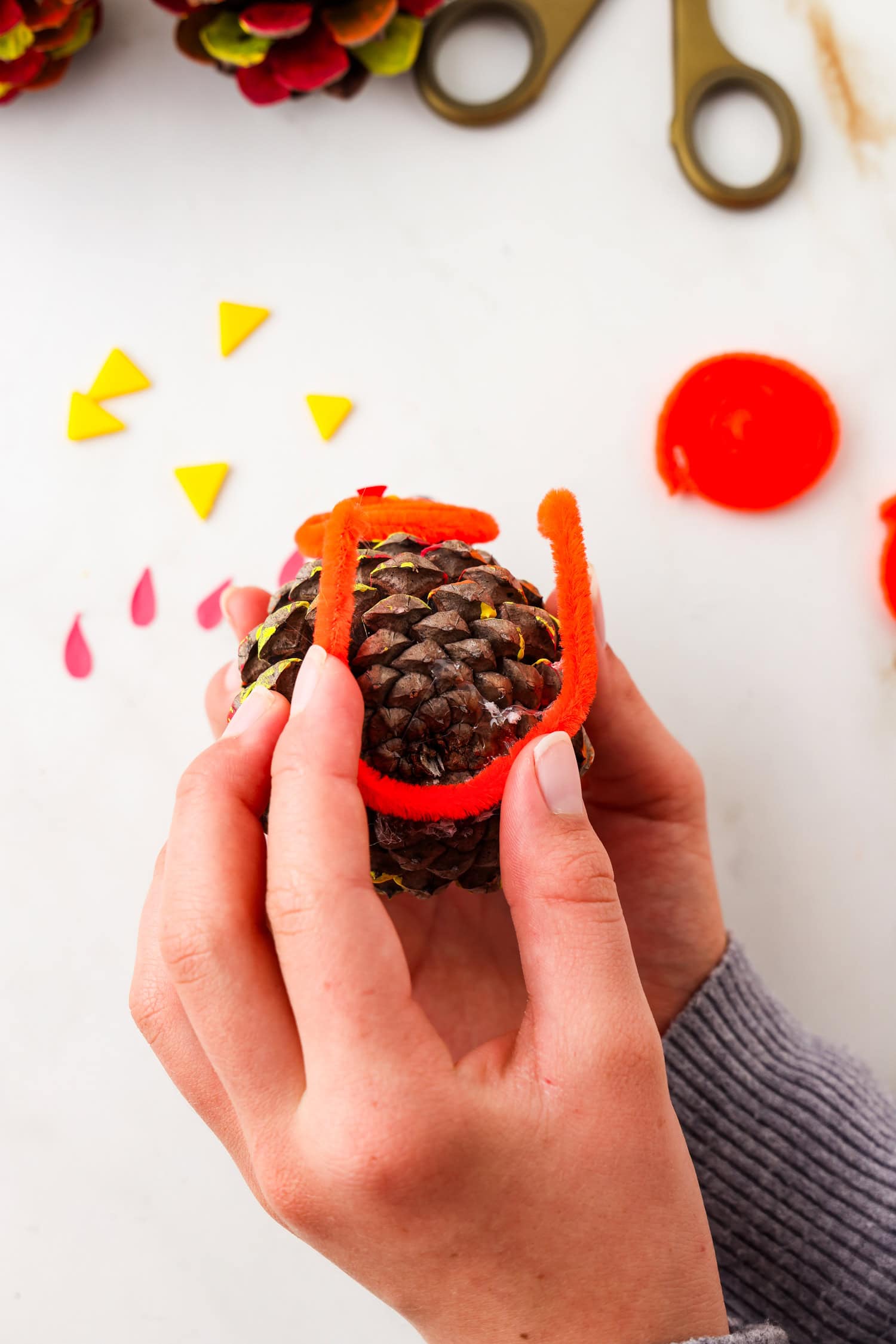 Picture of pipecleaner feet being glued to the bottom of pinecone.