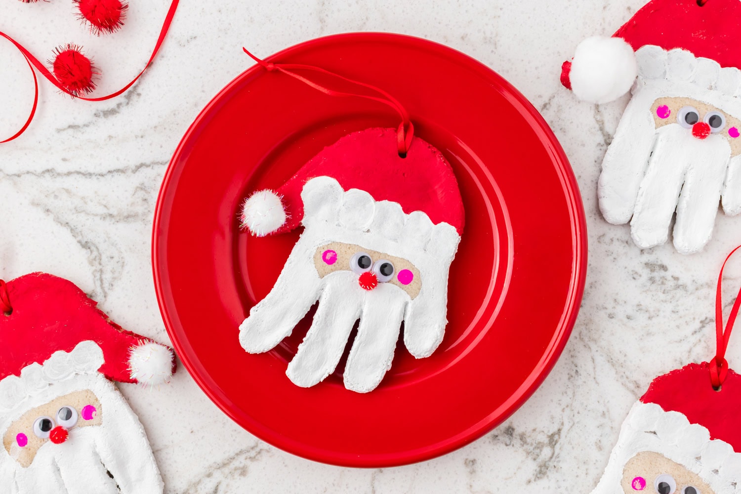 Close-up of a Santa handprint ornament on a red plate surrounded by more matching ornaments.