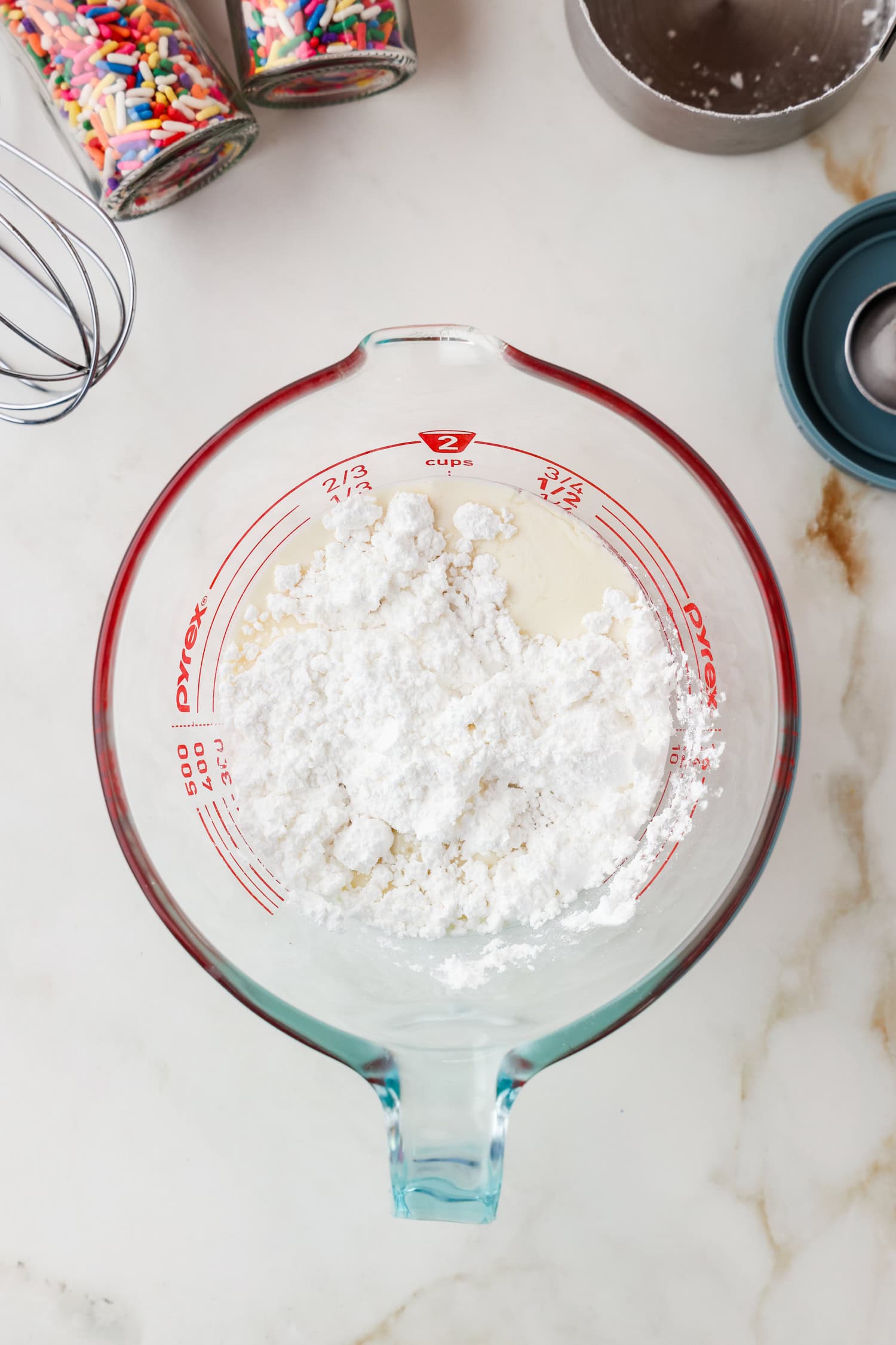 Glass measuring bowl with heavy cream and powdered sugar in it.