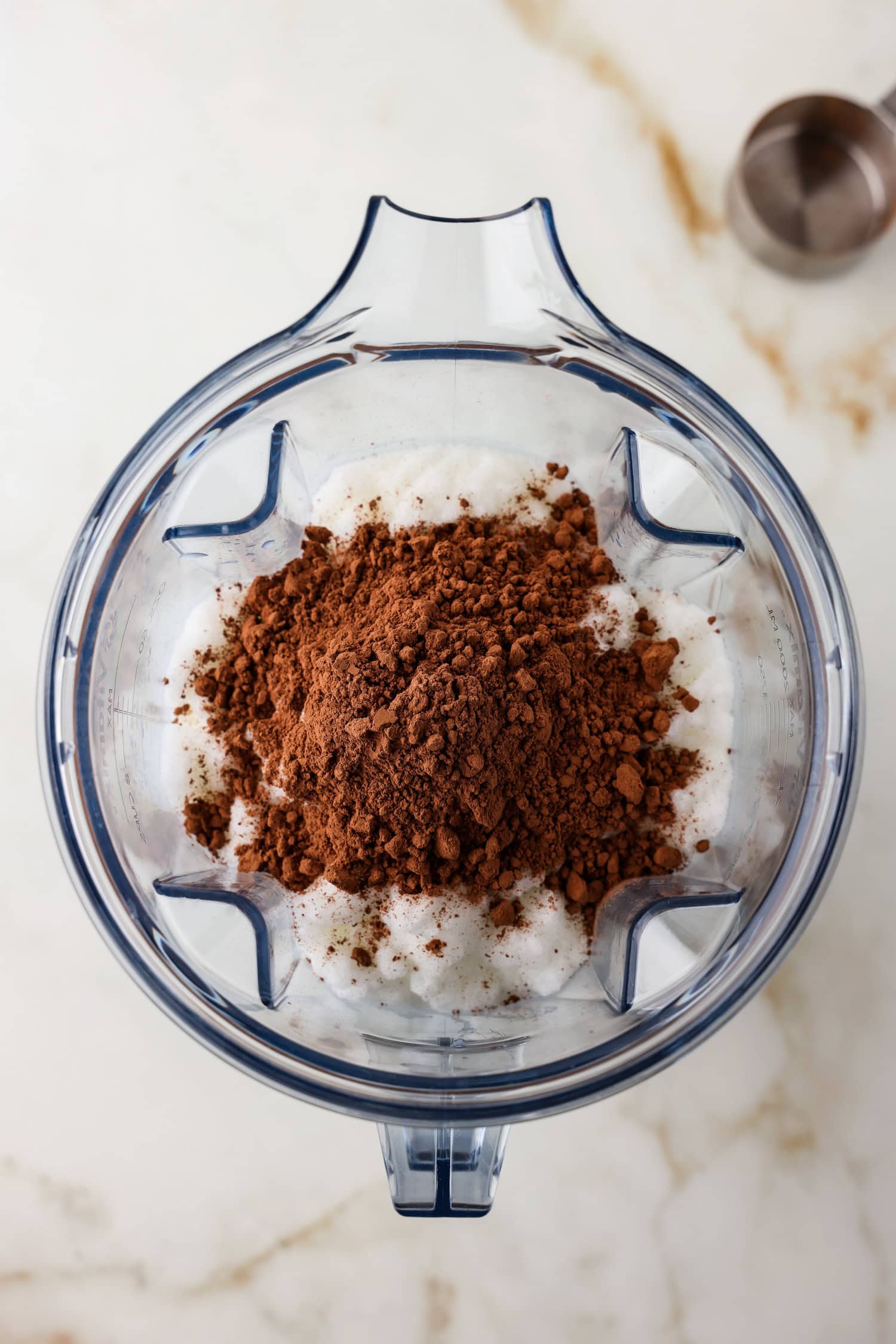 Overhead picture of cocoa powder being added to snow ice cream in a blender.