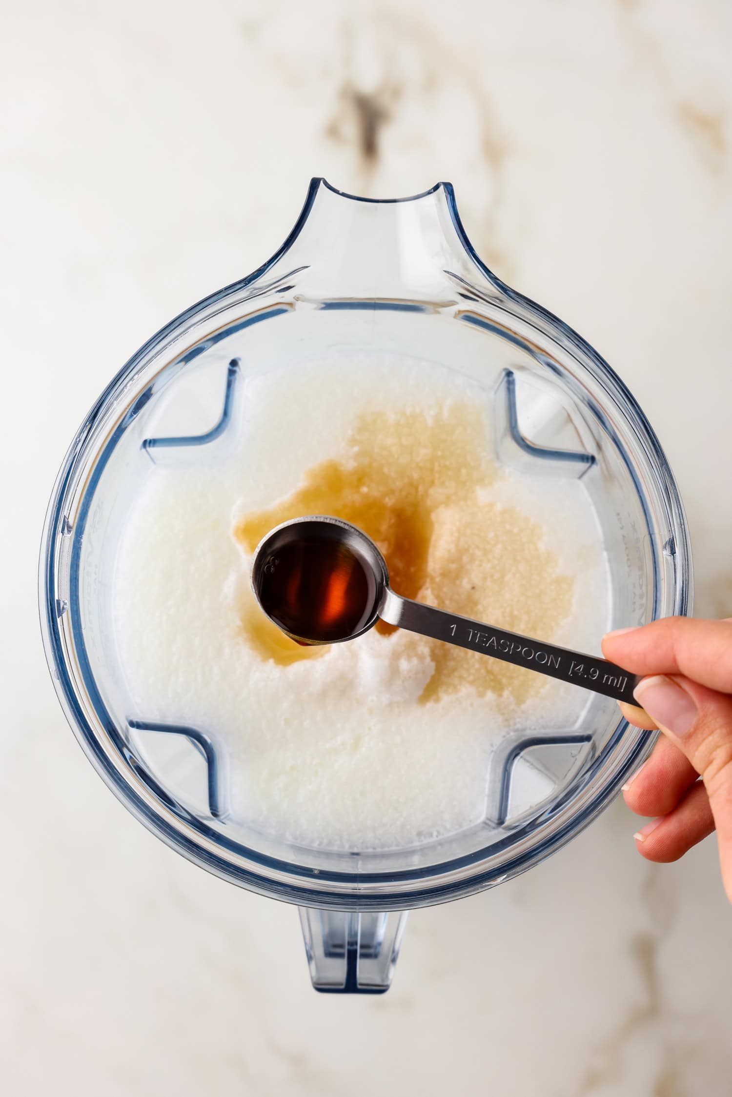 Overhead picture of vanilla being added to snow ice cream in a blender.