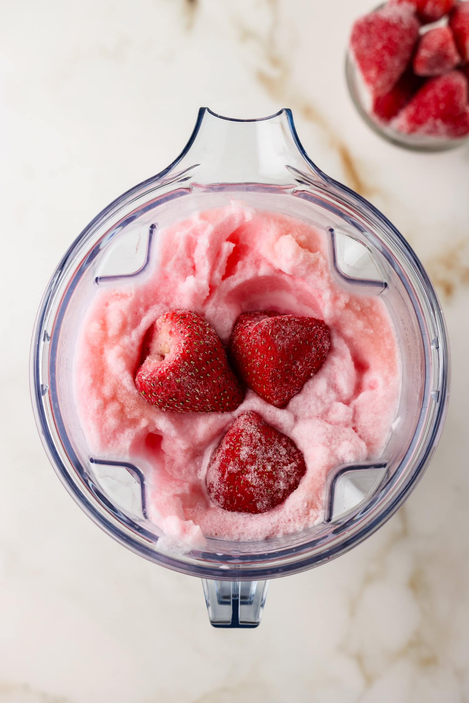 Overhead picture of strawberrys being added to snow ice cream in the blender.