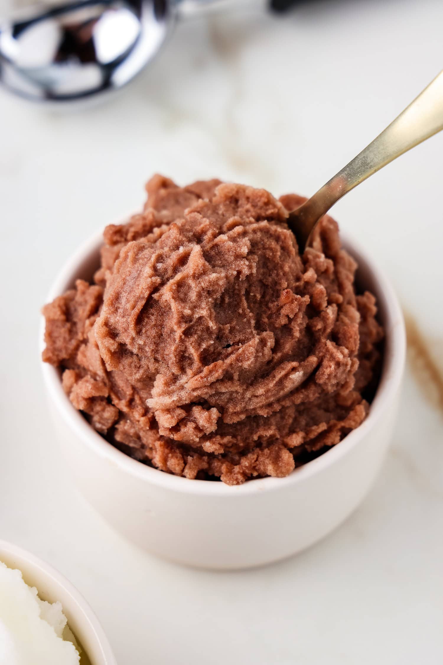 Chocolate snow ice cream in a white dish with a spoon in it.
