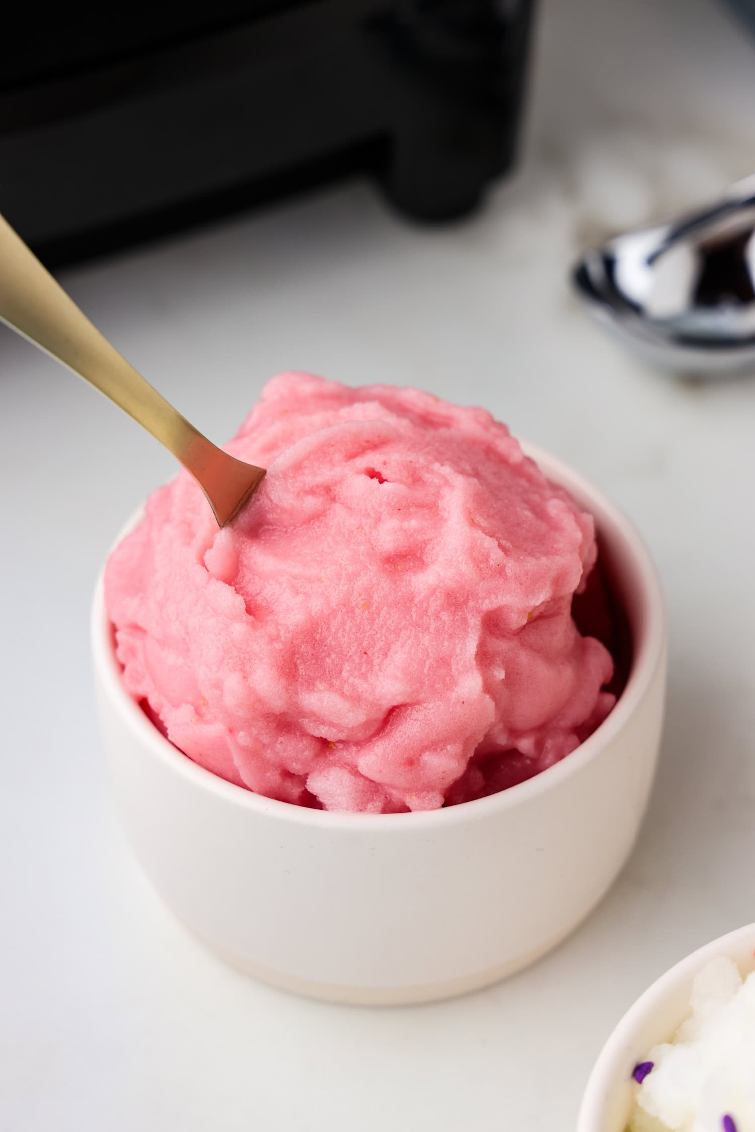 Strawberry snow ice cream in a white dish with a spoon in it.