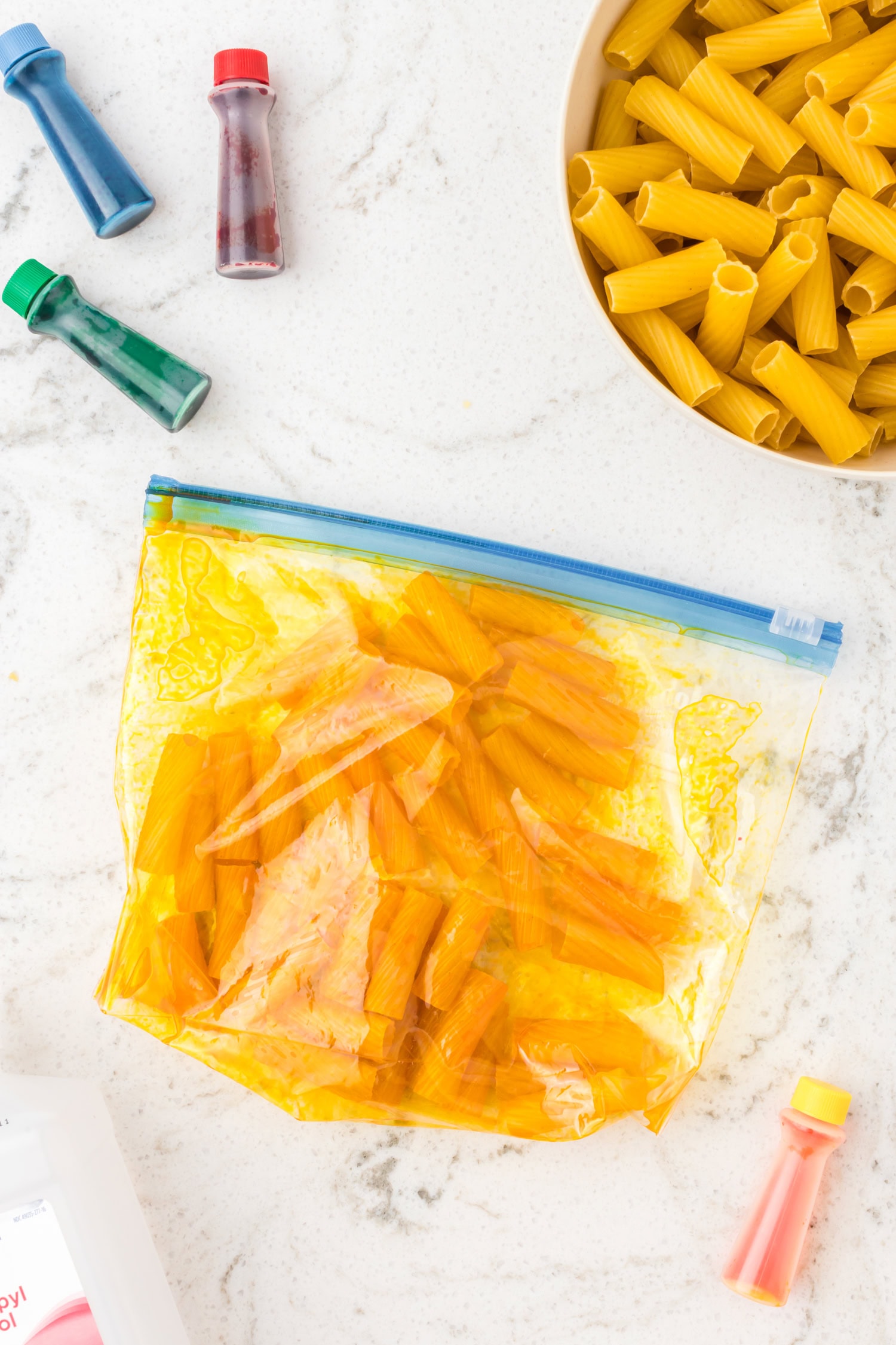 Zip-top bag filled with freshly dyed yellow and orange pasta drying after coloring.
