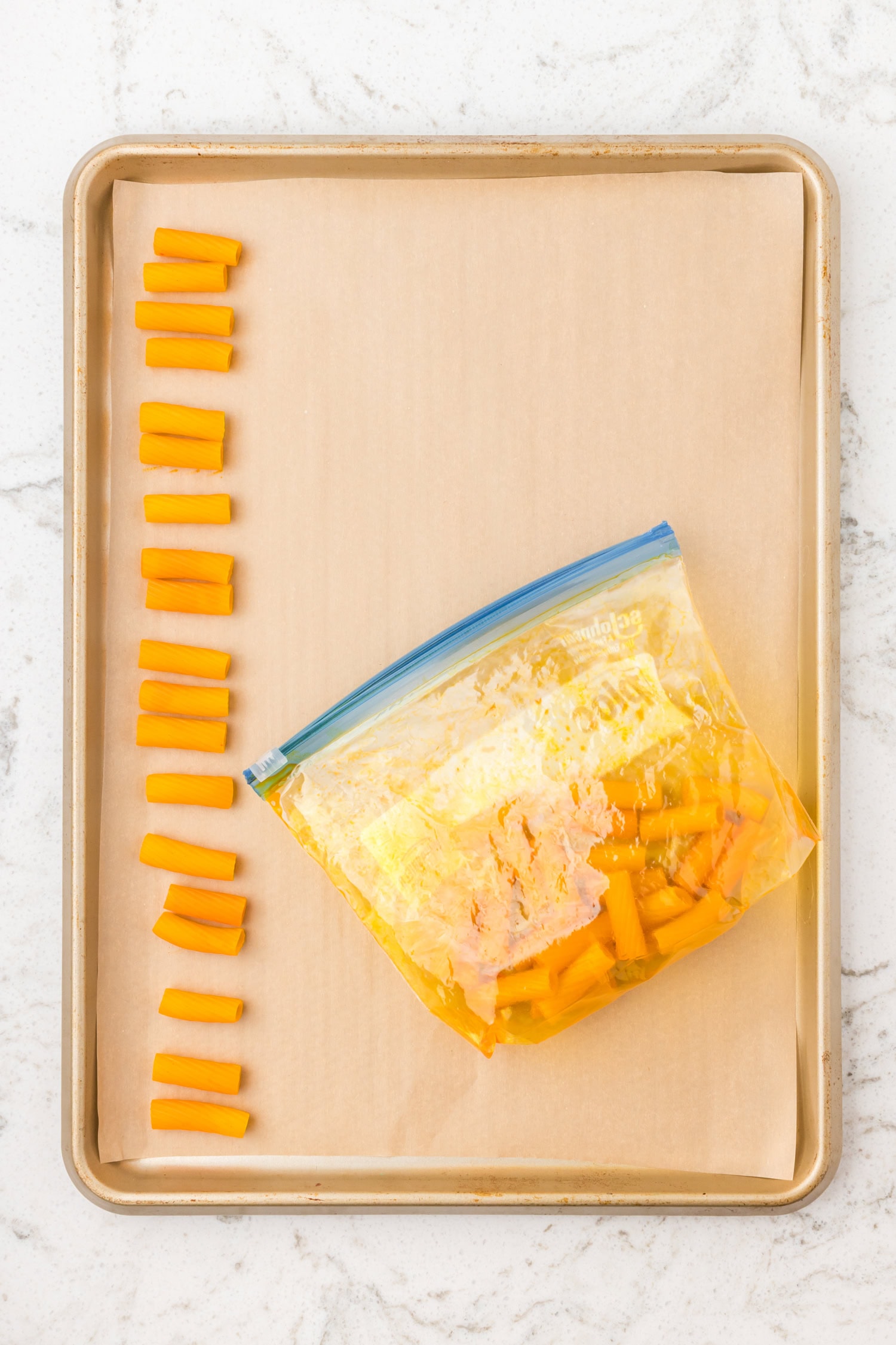 Dyed pasta pieces spread on a parchment-lined baking sheet to dry before making necklaces.