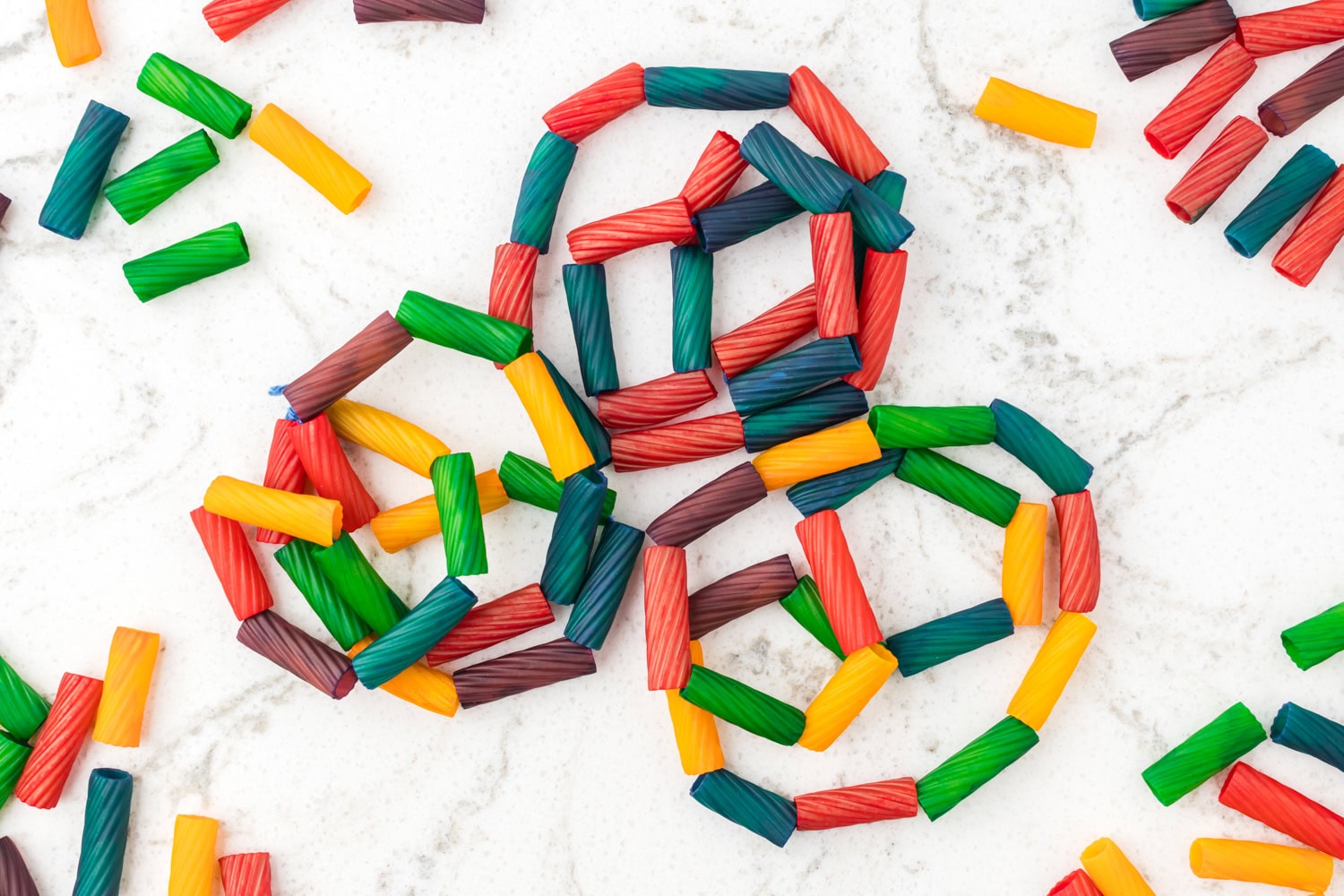 Finished pasta necklaces arranged on a white surface with colorful pasta beads scattered around.
