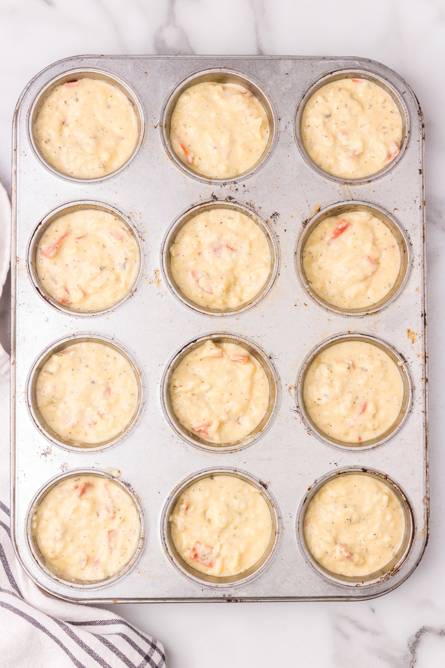 Muffin tin filled with raw pizza muffin batter portioned evenly into each cup before baking.