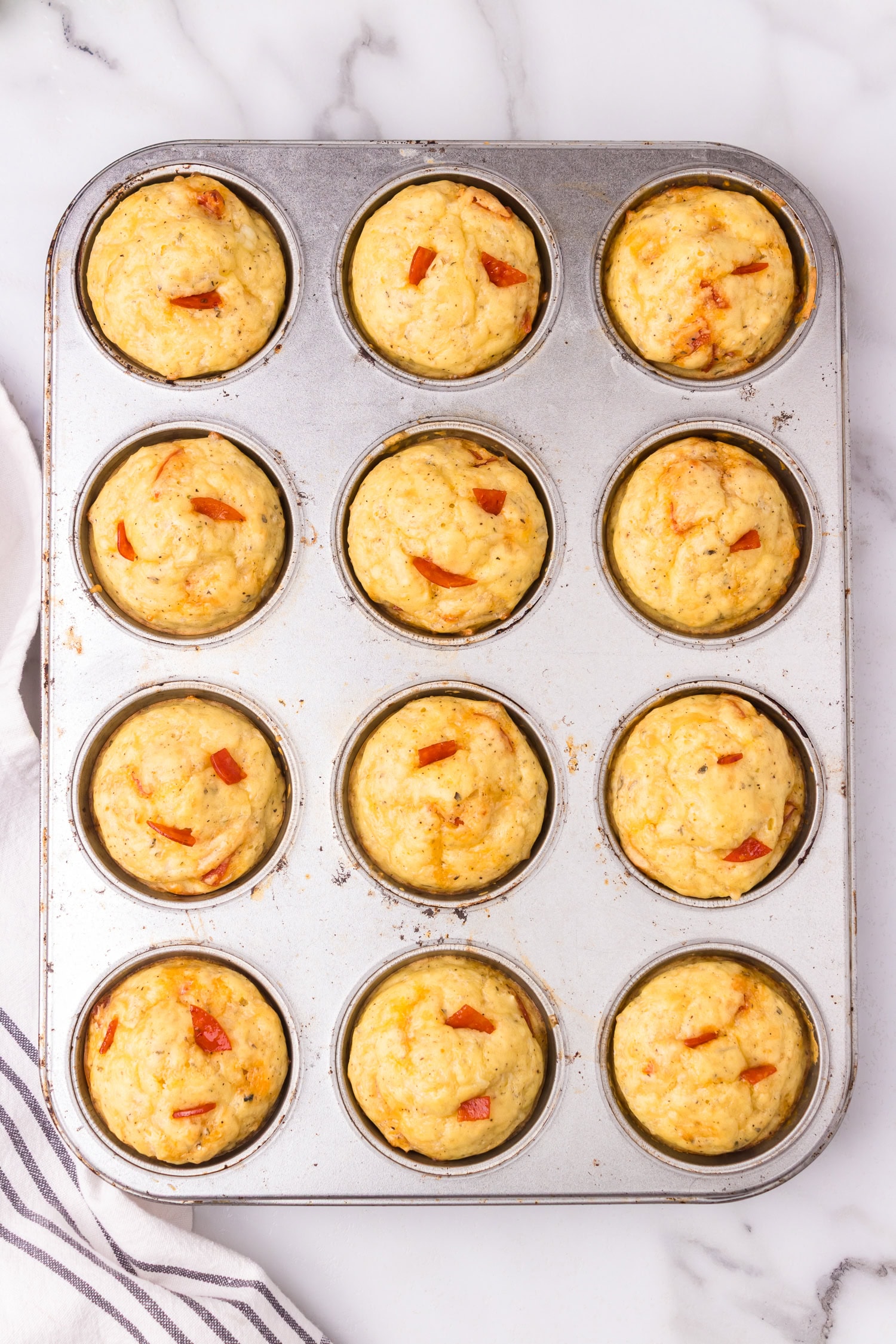 Freshly baked pizza muffins in a metal muffin pan, golden brown with small pieces of pepperoni visible on top.