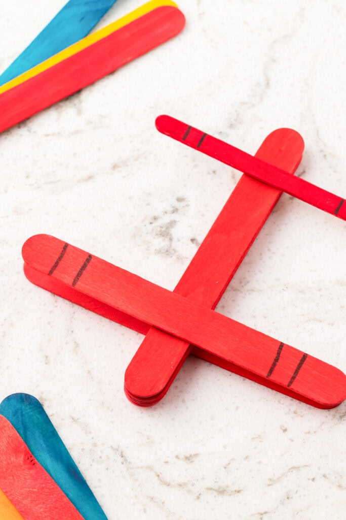 Close-up of a red popsicle stick airplane with black stripe details on a white marble surface.