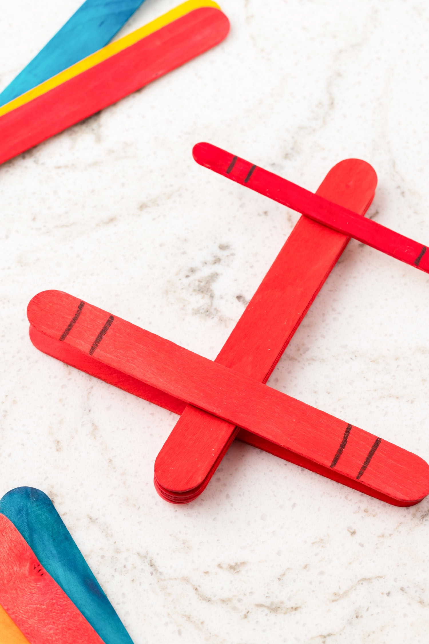 Close-up of a red popsicle stick airplane with black stripe details on a white marble surface.