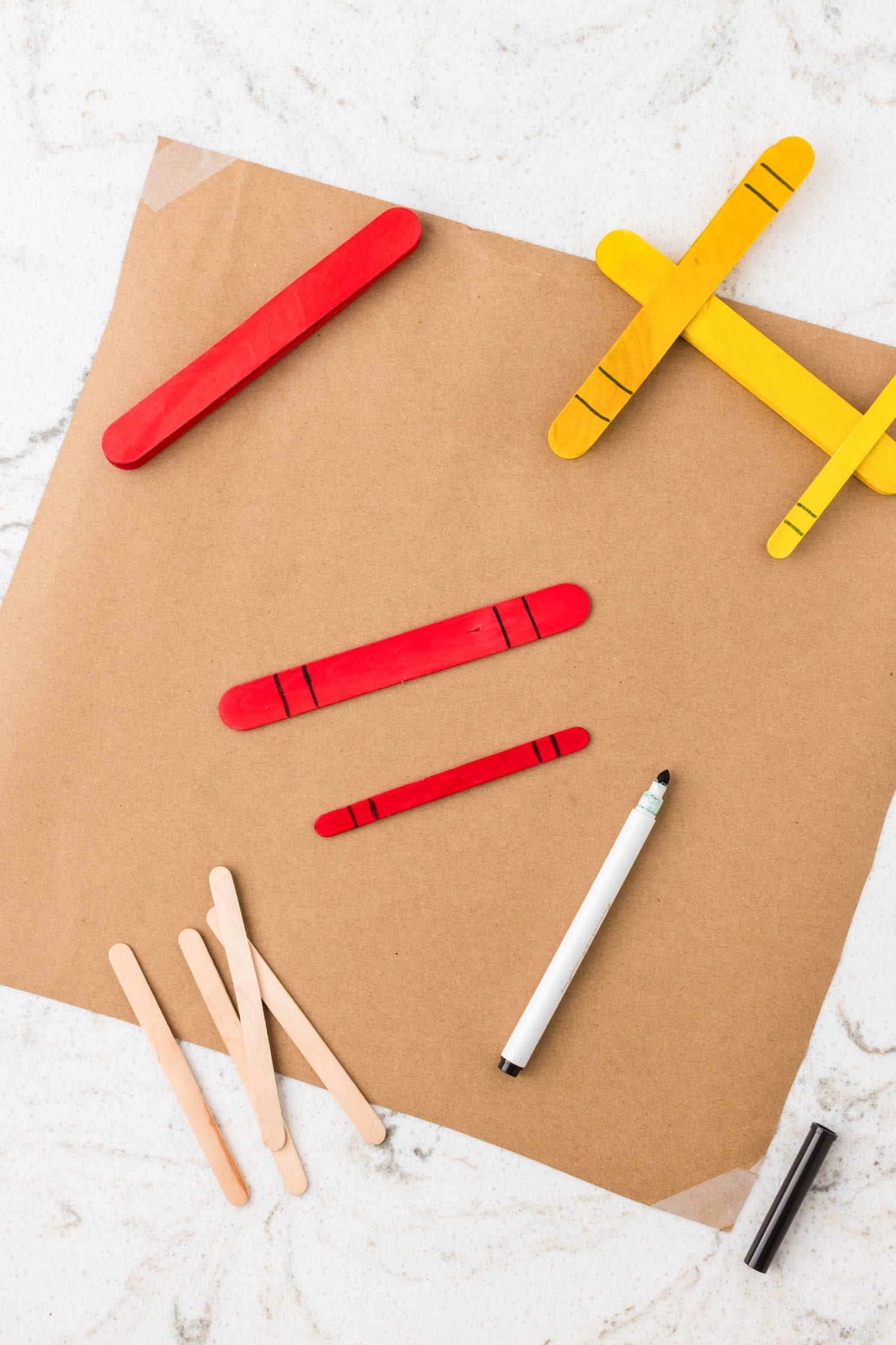 Blue, red, and yellow popsicle stick airplanes arranged on brown paper, with a bottle of school glue nearby.