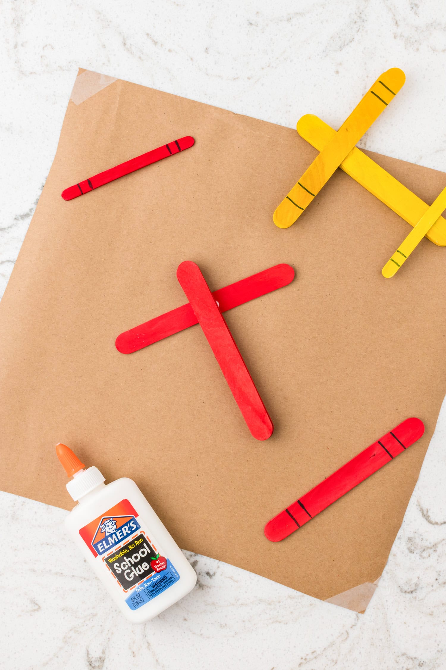 Painted red popsicle sticks with black marker details laid out on brown craft paper next to a marker and unpainted sticks.