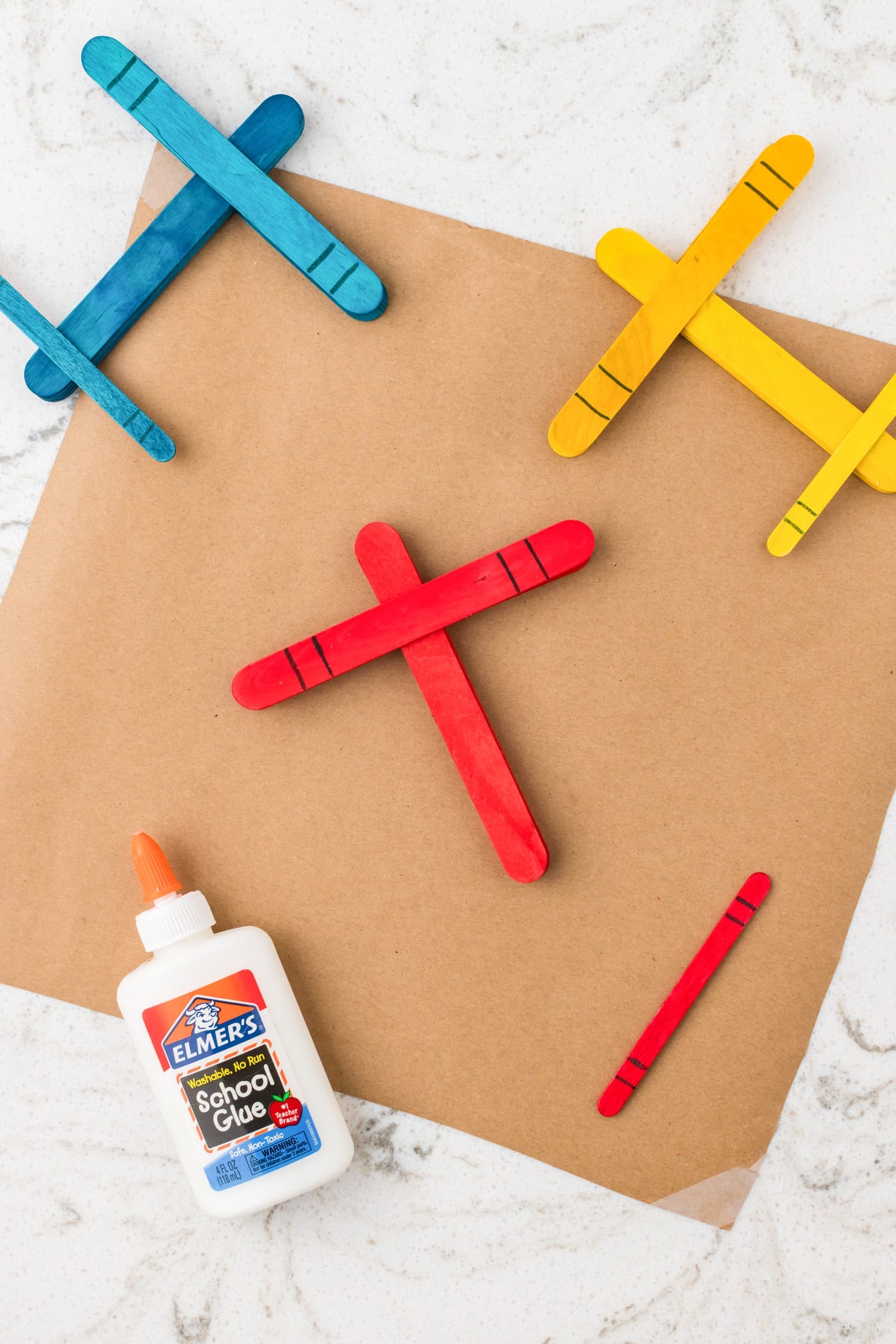 Red and blue painted popsicle stick airplanes assembled in a crisscross design on a marble background.