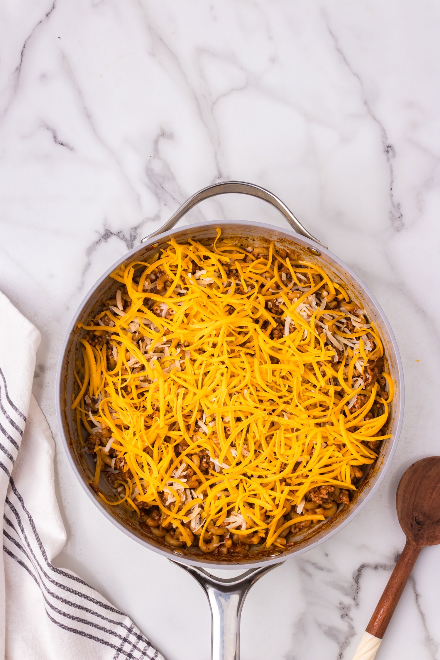 Beef and macaroni mixture in a skillet topped with shredded cheddar and mozzarella cheese before melting.