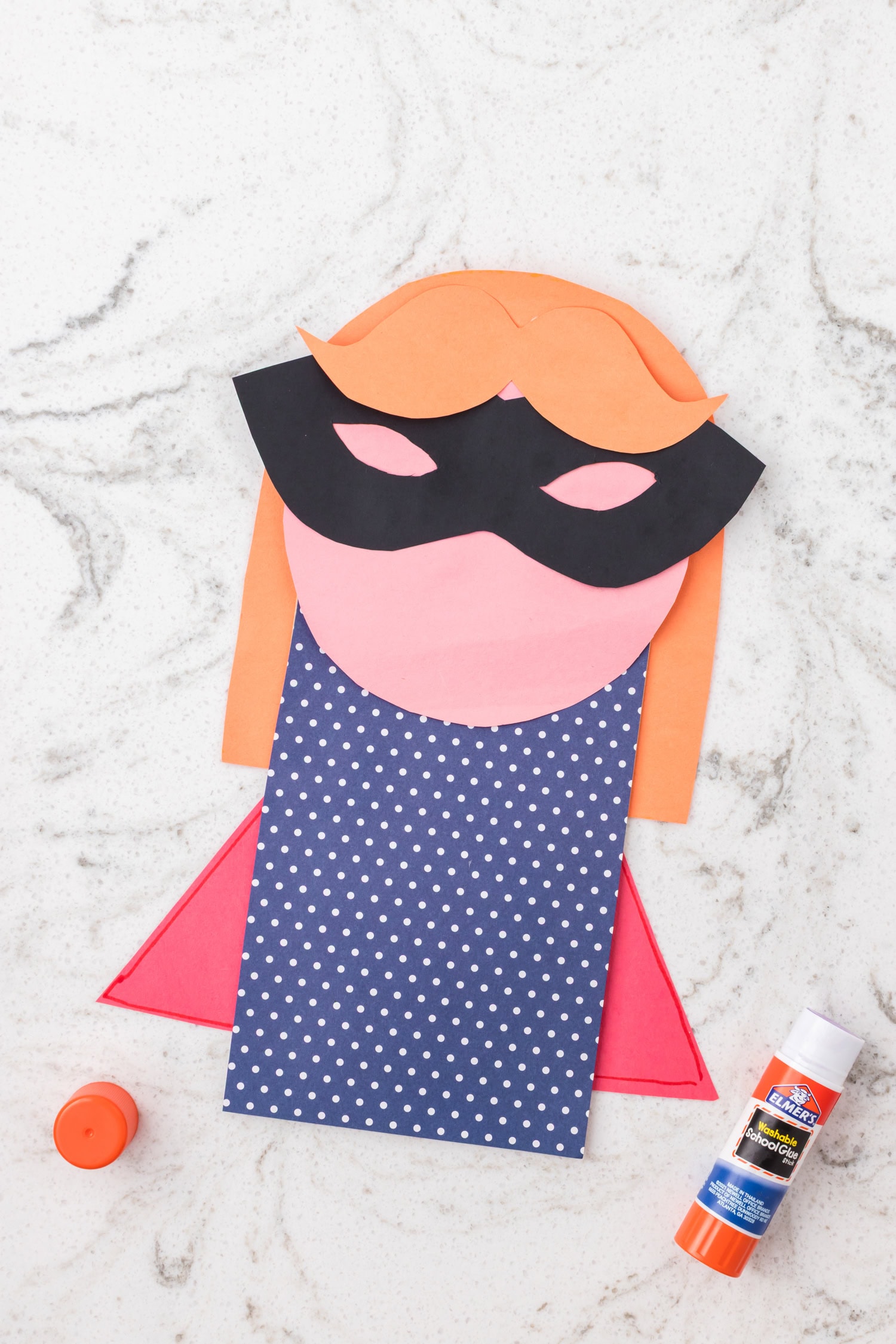 Paper superhero craft with black mask and orange hair added to the face on a decorated paper bag.