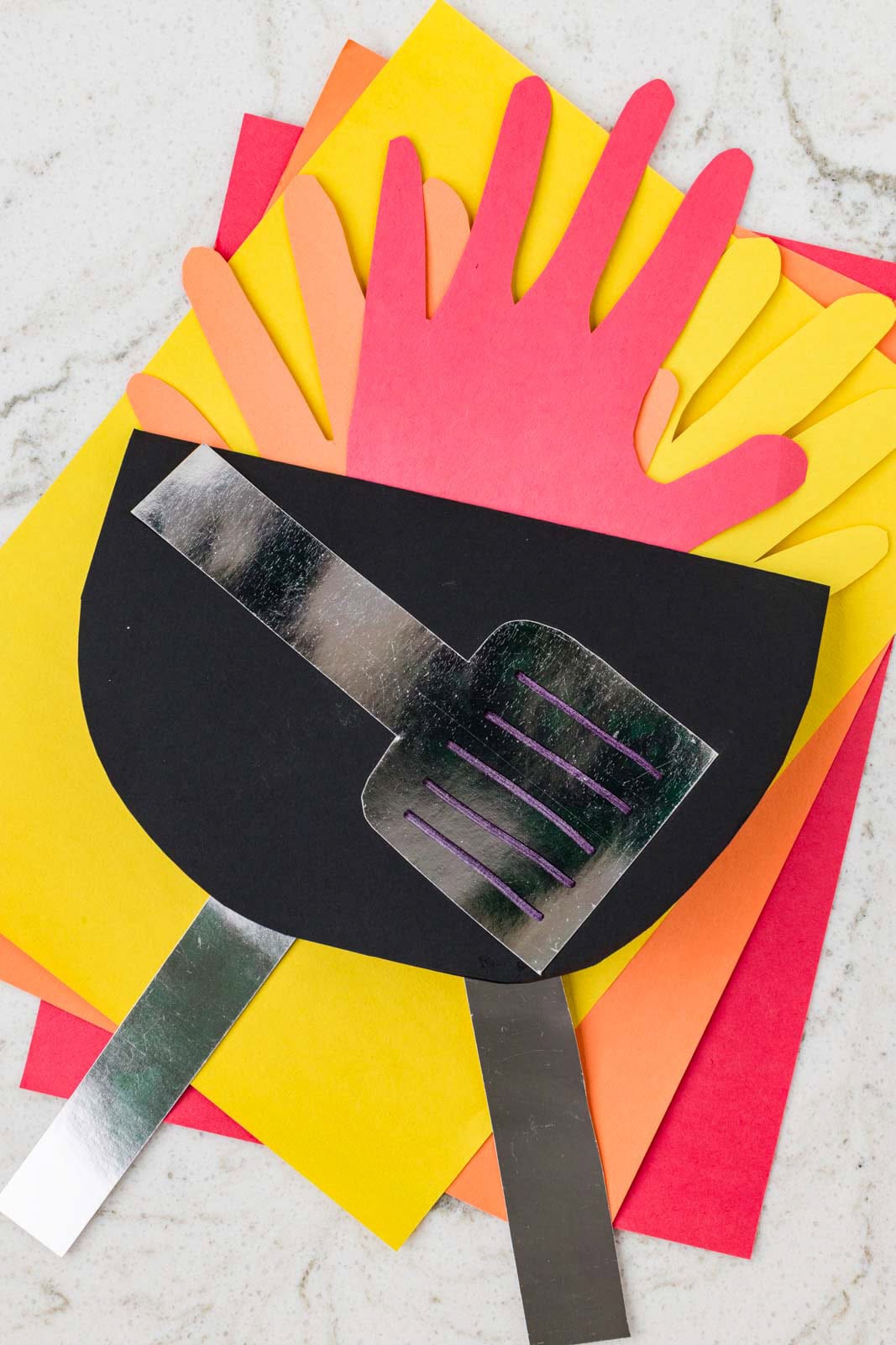 Completed grill craft with paper handprint flames and a spatula design layered on colored paper.