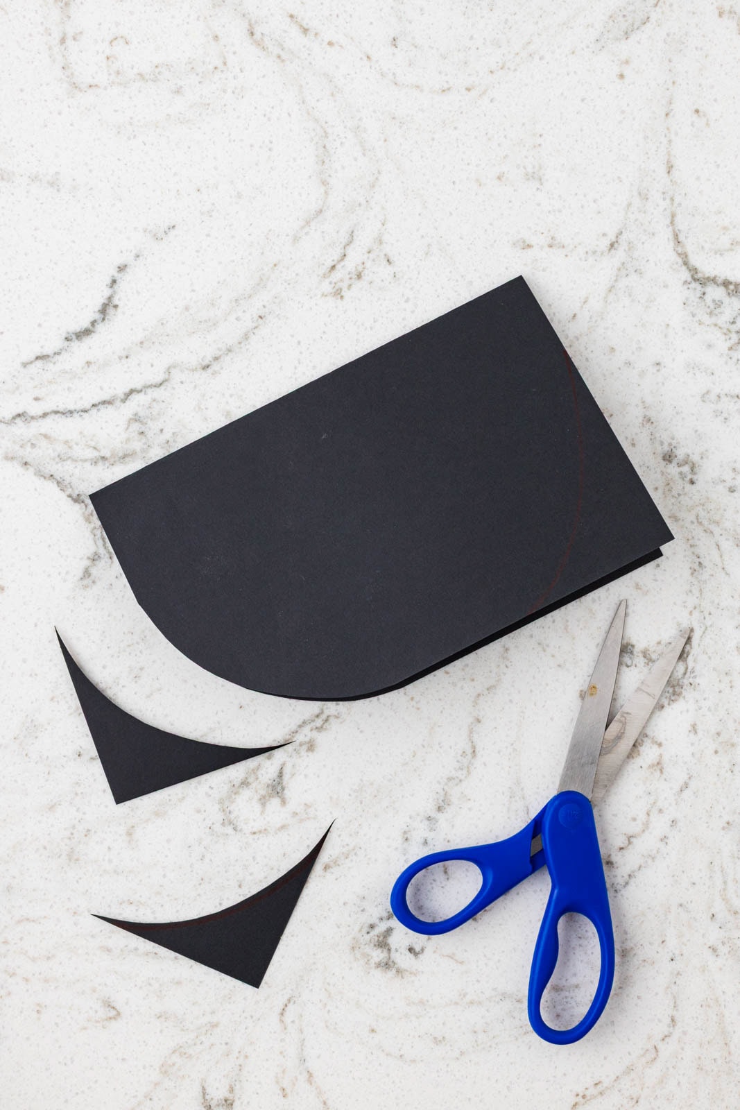Black cardstock being cut into a rounded grill shape with scissors on a marble surface.