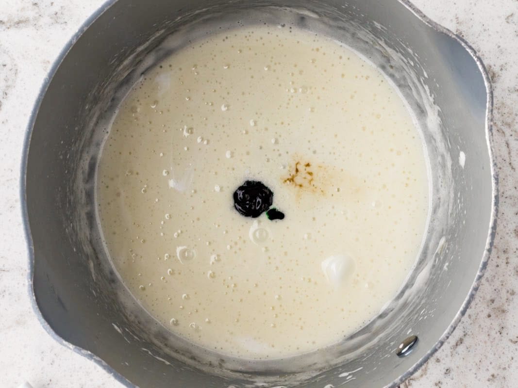 Overhead view of melted marshmallow mixture in a saucepan with green food coloring being added to create watermelon-themed Rice Krispies treats.