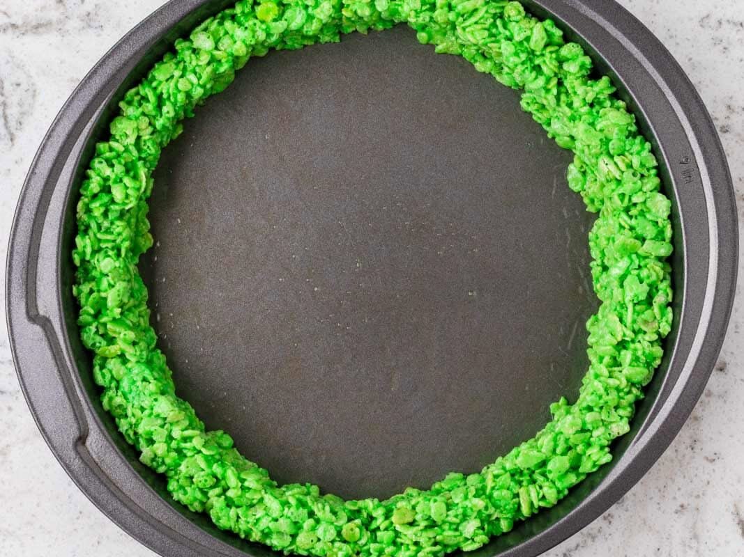 Round cake pan lined with a bright green Rice Krispies treat layer pressed around the outer edge to resemble a watermelon rind.