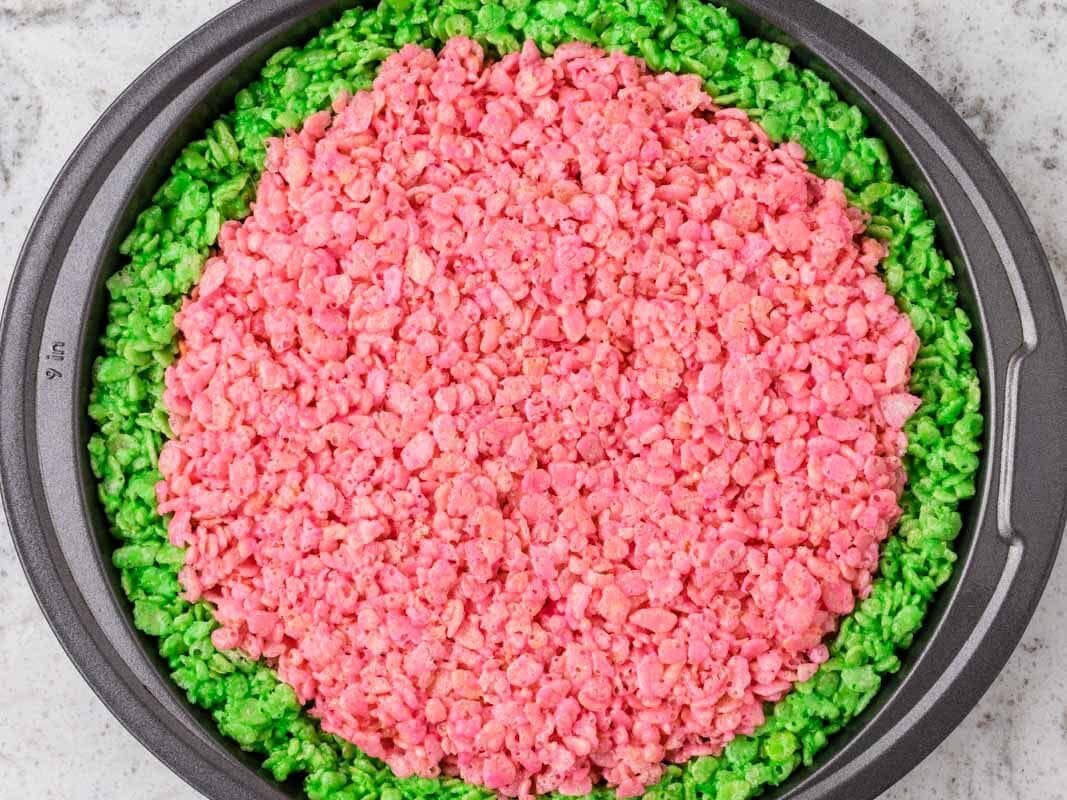 Pink Rice Krispies treat mixture pressed into the center of a round pan, surrounded by a green Rice Krispies rind to create a watermelon design.