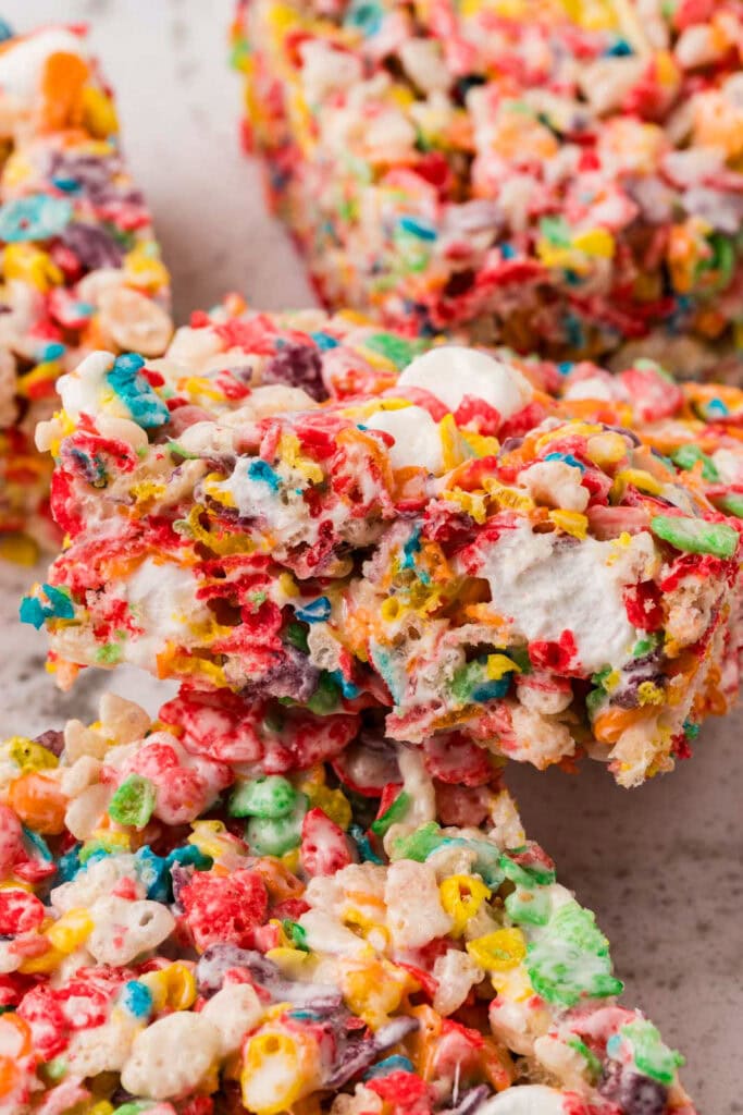 Close-up of rainbow Rice Krispies treats packed with colorful fruity cereal, mini marshmallows, and candy pieces held together with gooey marshmallow.