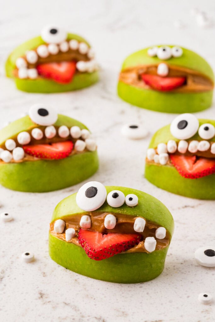 Close-up of a healthy Halloween apple monster snack made with a green apple, peanut butter, a strawberry tongue, mini marshmallow teeth, and candy eyes.