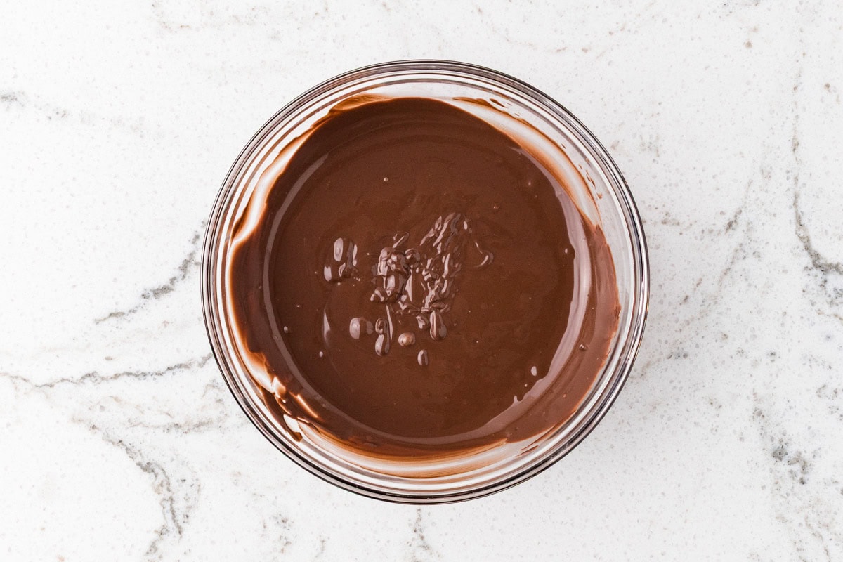 Bowl of smooth melted chocolate on a light marble surface, ready for decorating Halloween spider donuts.