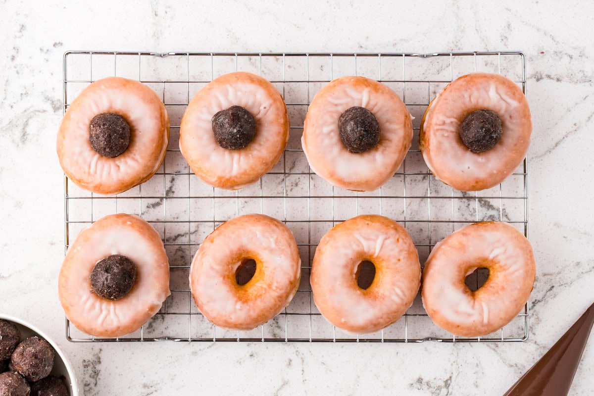 Glazed donuts on a cooling rack topped with chocolate truffle balls to create spider bodies.