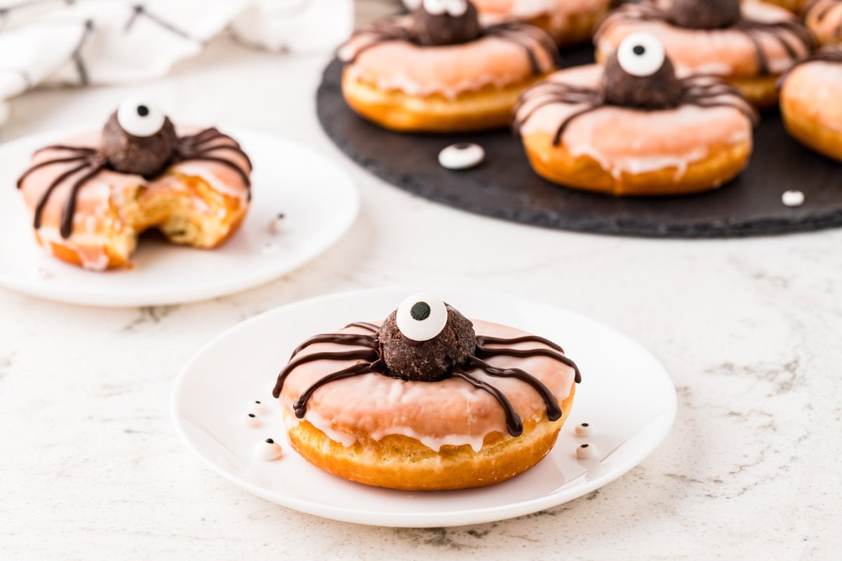 Overhead view of glazed Halloween spider donuts with chocolate truffle bodies, piped chocolate legs, and candy eyes.