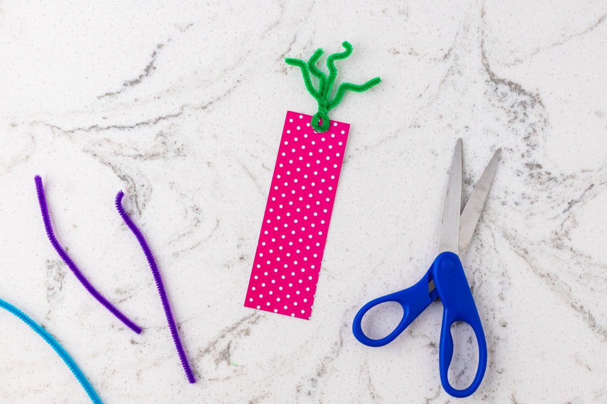 Pink polka-dot bookmark with green pipe cleaner tentacles attached through a hole at the top.