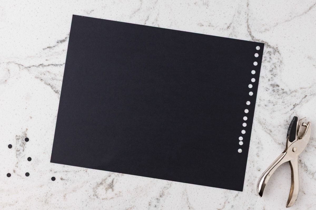 Black cardstock with small circles punched along one edge using a hole punch.